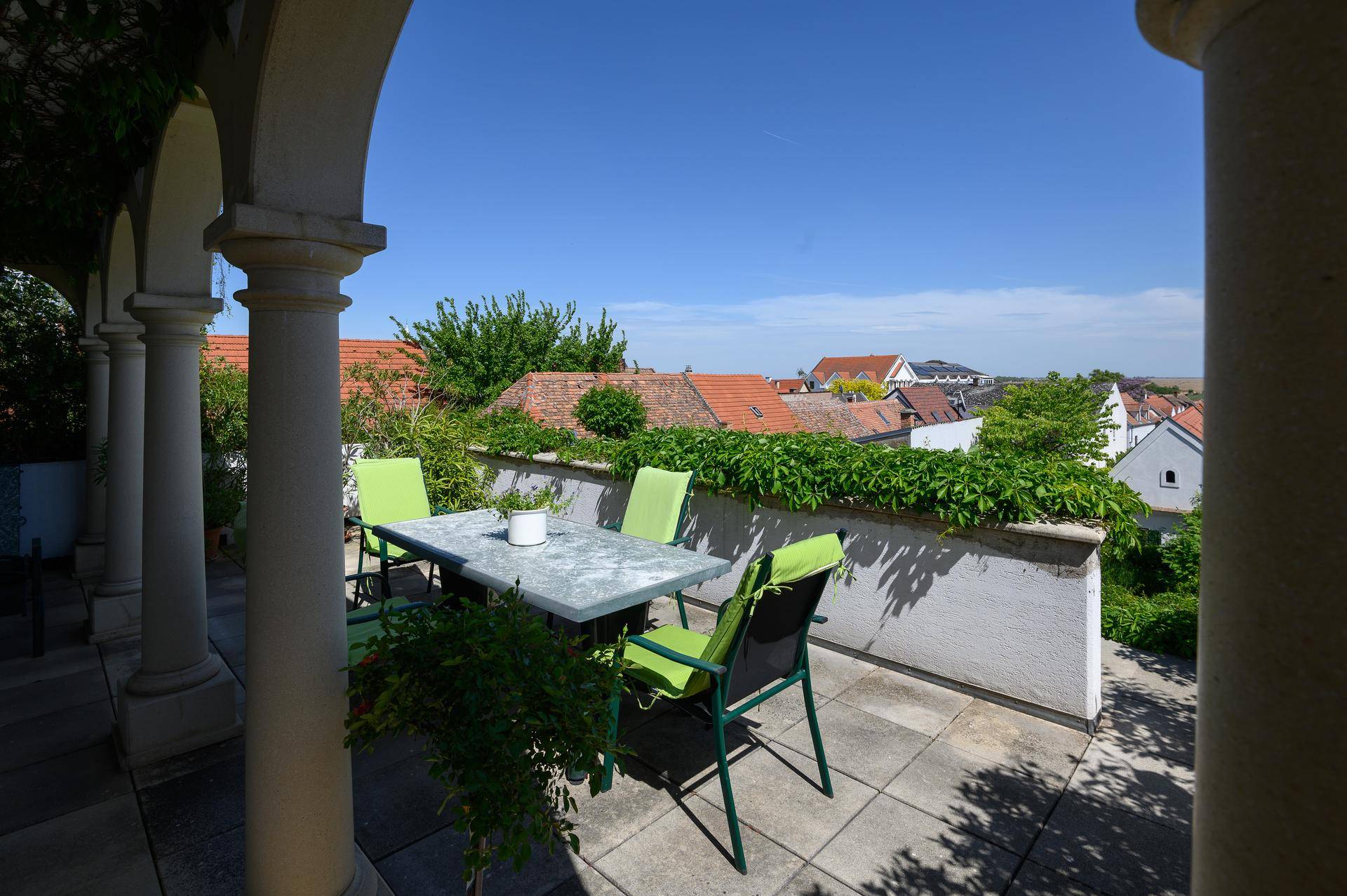 Sonniger Terrassenbereich mit Gartenmöbeln und Blick über die Dächer der umliegenden Häuser.