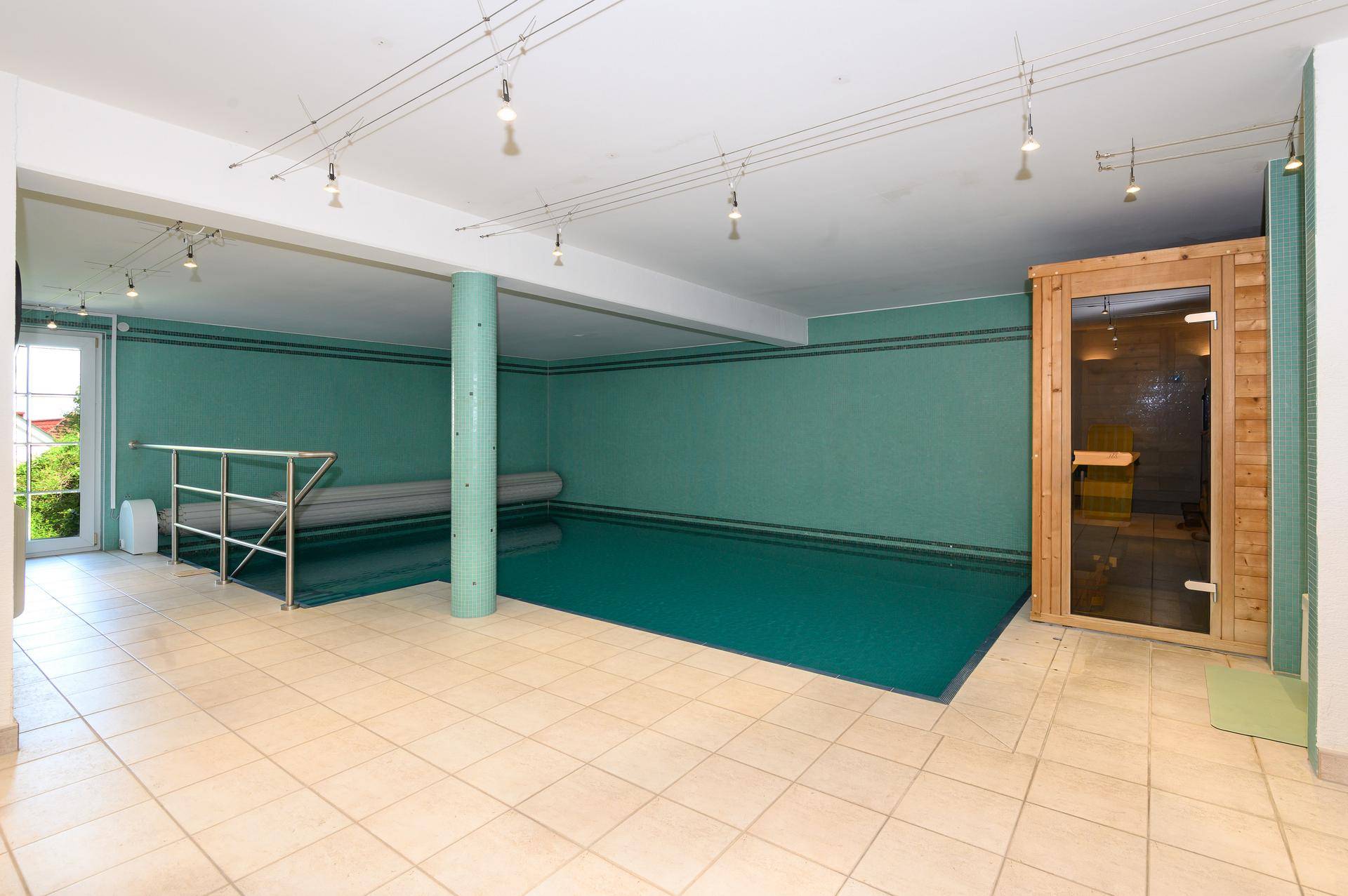 Innenpoolbereich mit Sauna, Fliesenboden und großem Fenster, ideal für Entspannung und Sport.