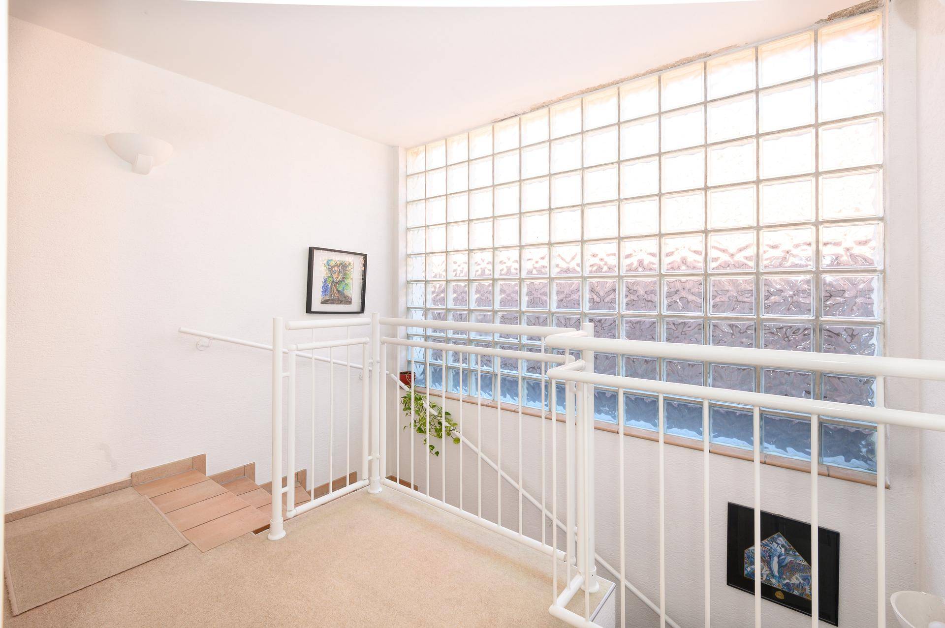 Heller Flurbereich mit Treppe und einer Wand aus Glasbausteinen, die für viel Tageslicht sorgt.
