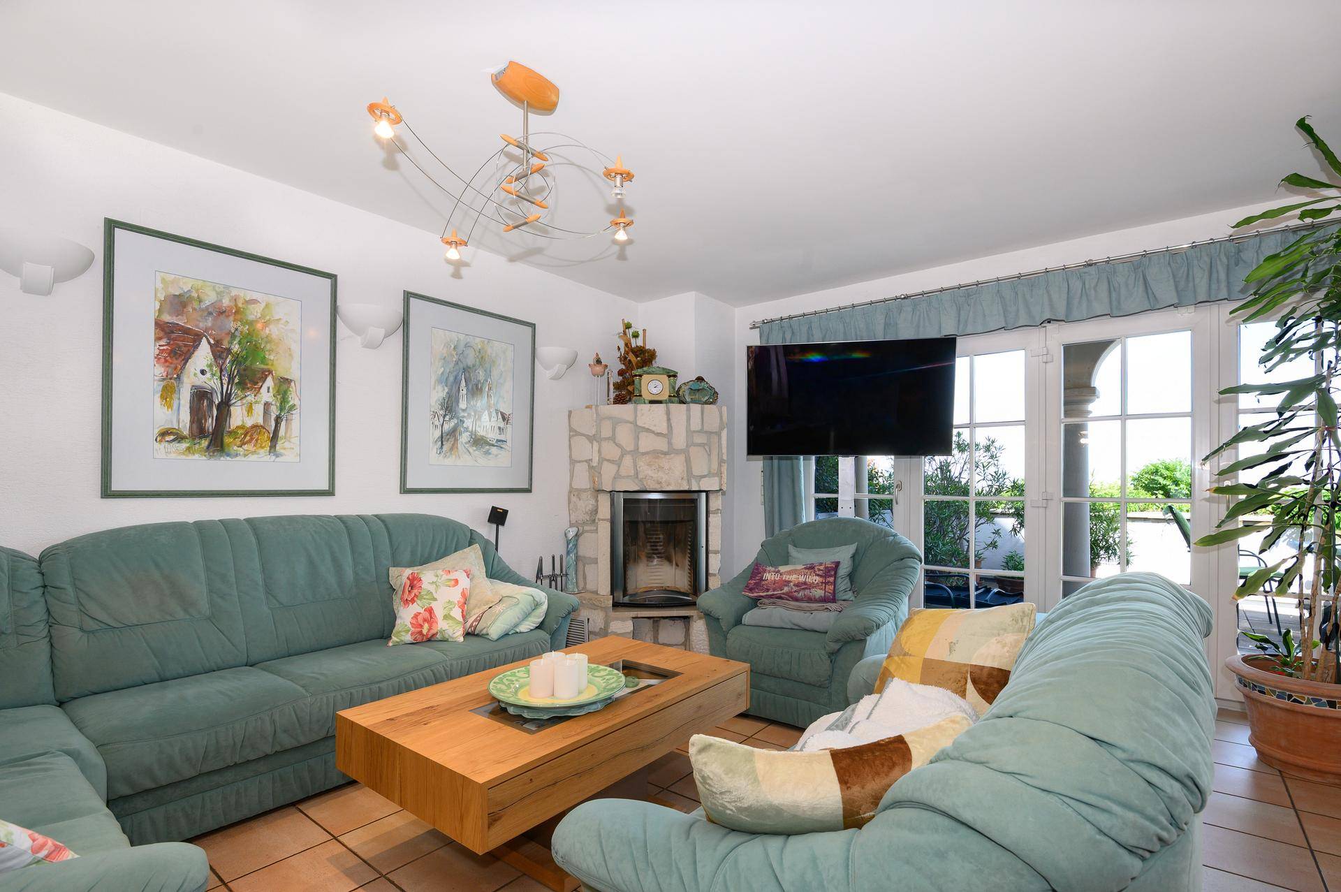 Gemütliches Wohnzimmer mit Kamin, bequemen Sofas und großen Fenstertüren, die viel Licht hereinlassen.