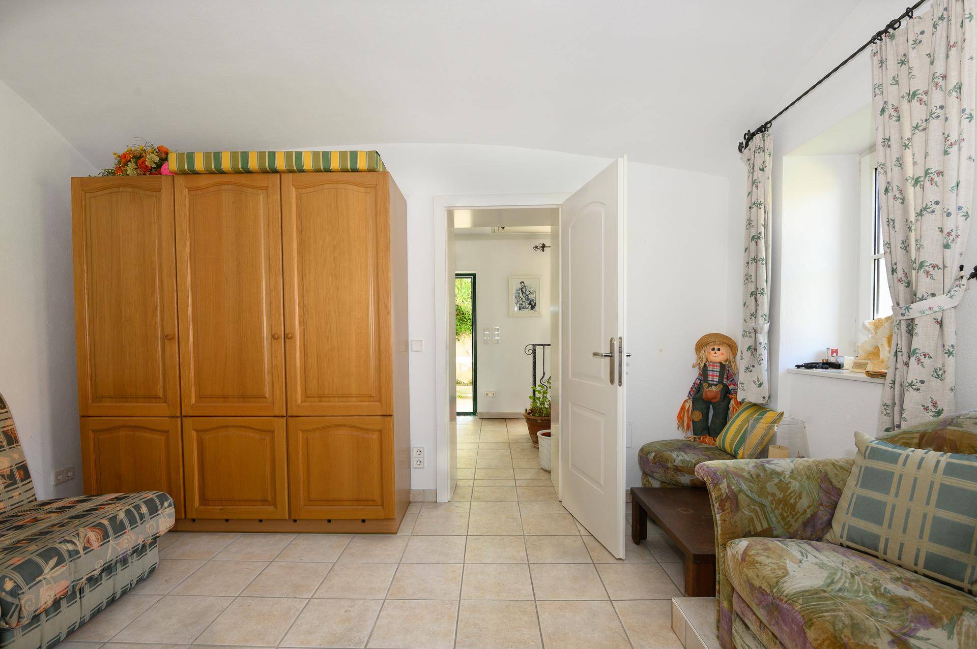 Heller Raum mit großem Holzschrank, Fliesenboden und Zugang zu einem weiteren Bereich des Hauses.