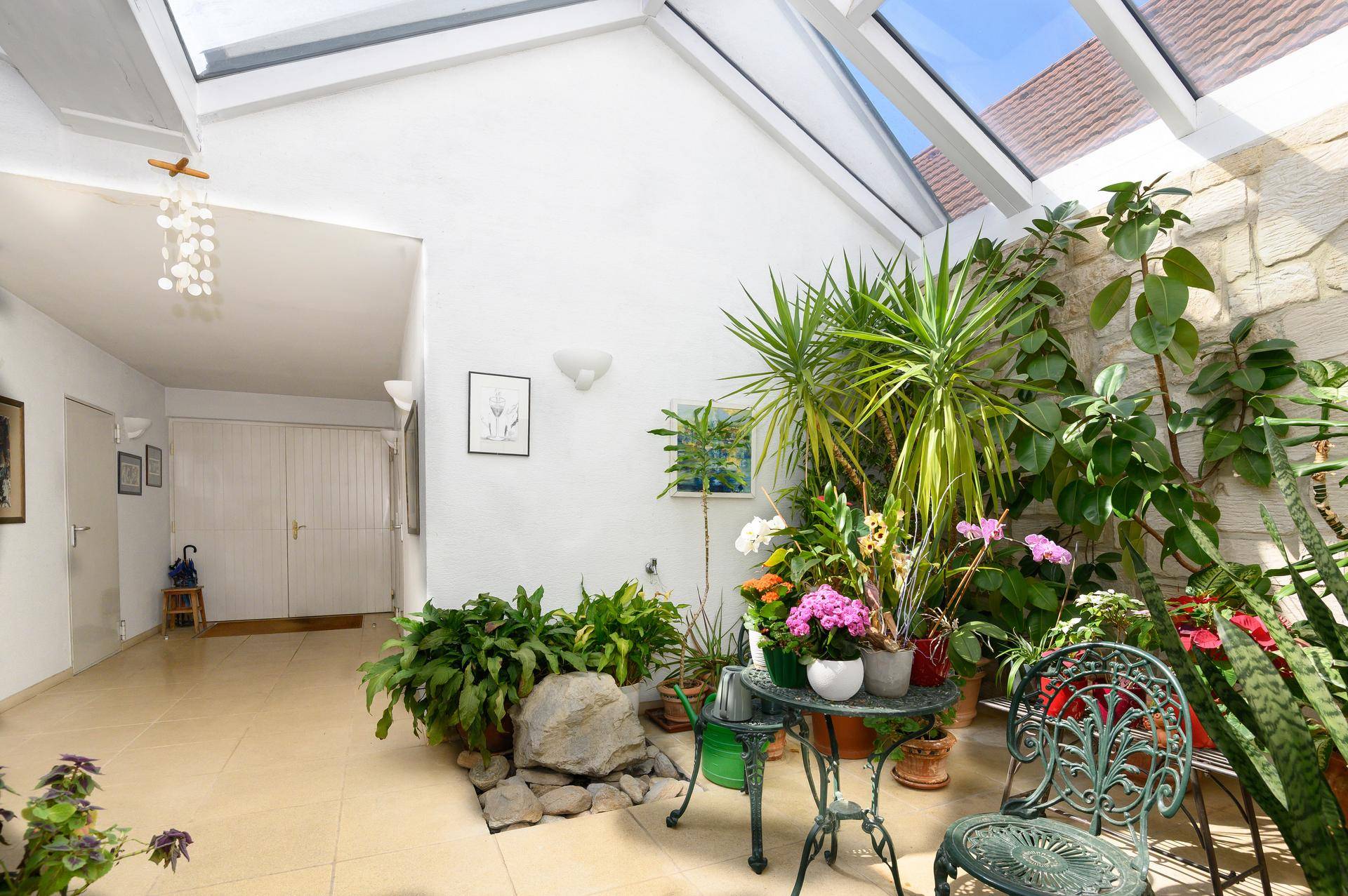 Heller Wintergarten mit Glasdach, vielen Pflanzen und einem kleinen Sitzbereich für entspannte Stunden.