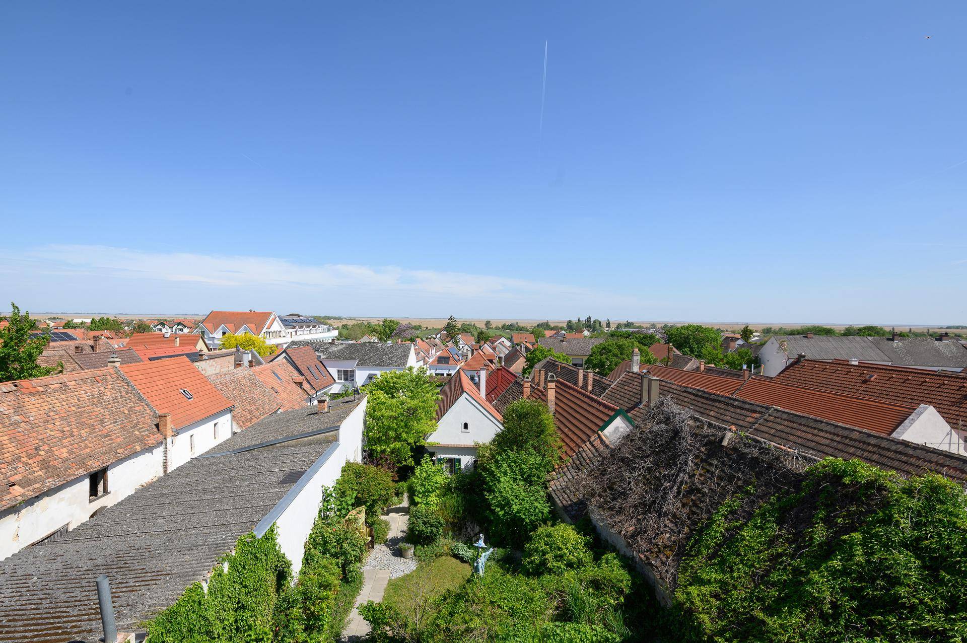 Weitblick über ein Dorf mit zahlreichen Dächern und grünen Gärten unter klarem blauem Himmel.