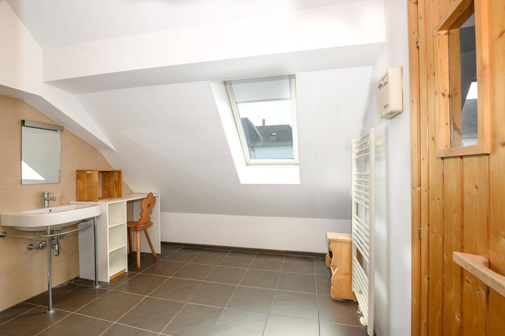 Dachgeschossraum mit Fliesenboden, Waschbecken, Handtuchheizkörper und integrierter Sauna.