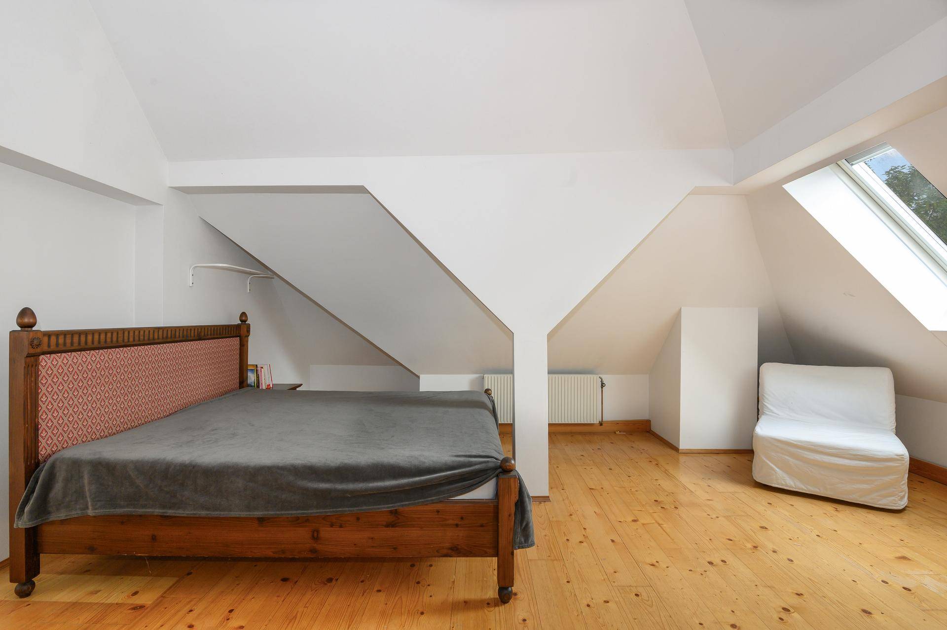 Schlafzimmer im Dachgeschoss mit Holzbett, Holzdielenboden und einem Dachfenster.