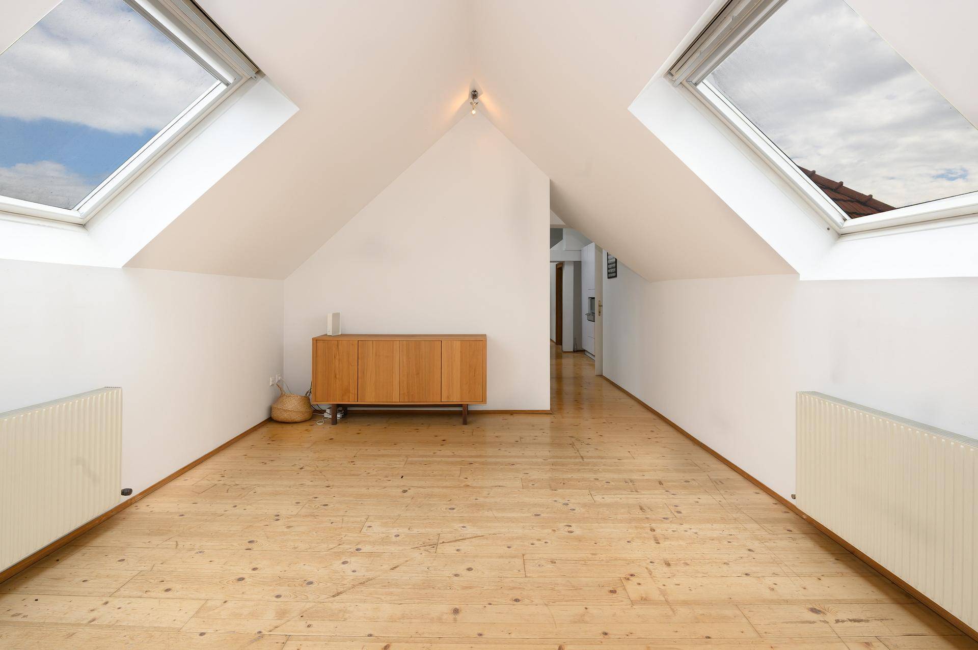 Heller Dachgeschossraum mit Holzdielenboden und zwei großen Dachfenstern.