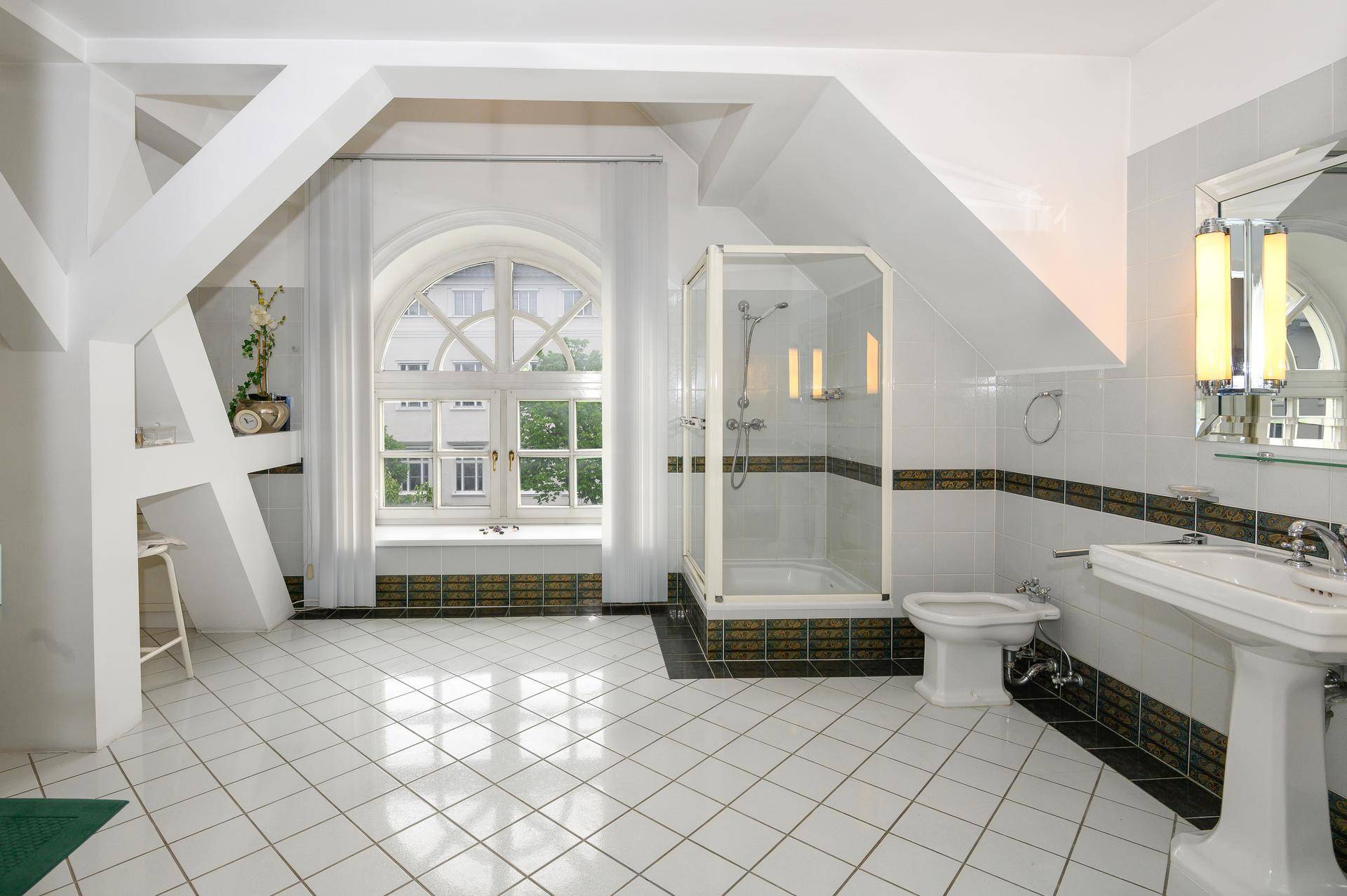 Helles Badezimmer im Dachgeschoss mit Duschkabine, Bidet und einem großen Rundbogenfenster.