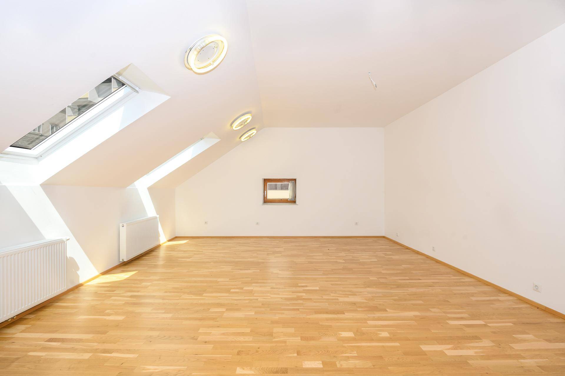 Heller Dachbodenraum mit Holzboden, Dachfenstern und Heizkörpern, ideal als Schlaf- oder Arbeitszimmer.