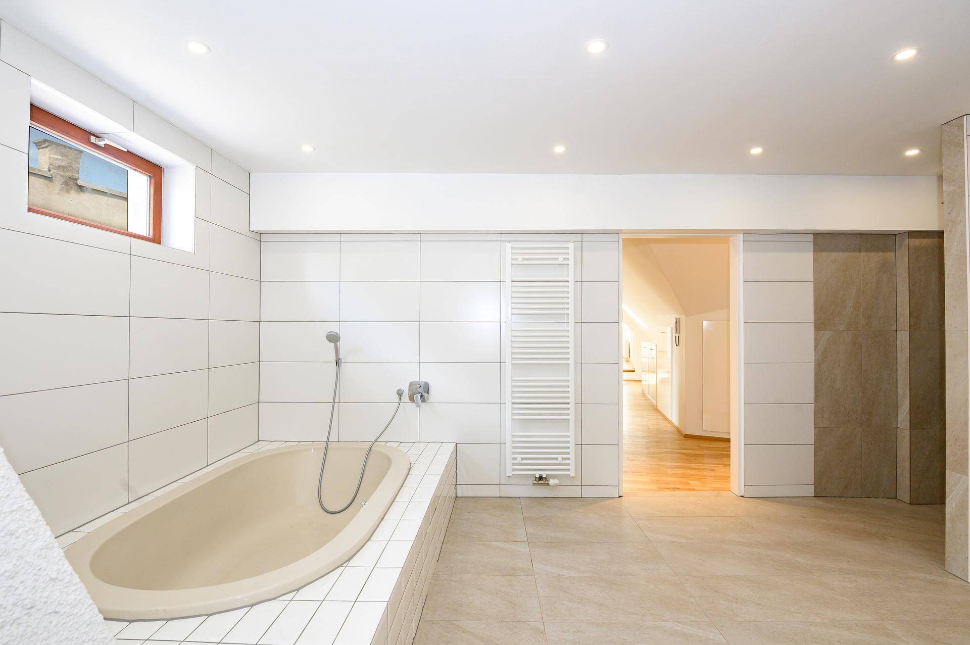 Modernes Badezimmer mit großer Badewanne, weißen Fliesen und einem beheizten Handtuchhalter.