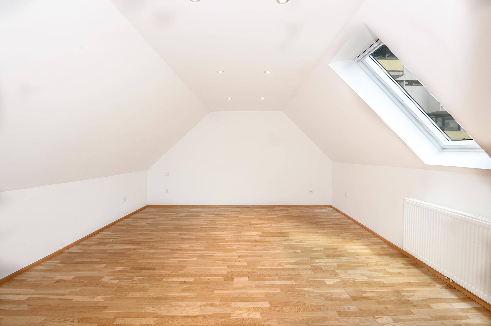 Heller Dachbodenraum mit Holzboden, einem großen Dachfenster und Heizkörpern, ideal für individuelle Gestaltung.