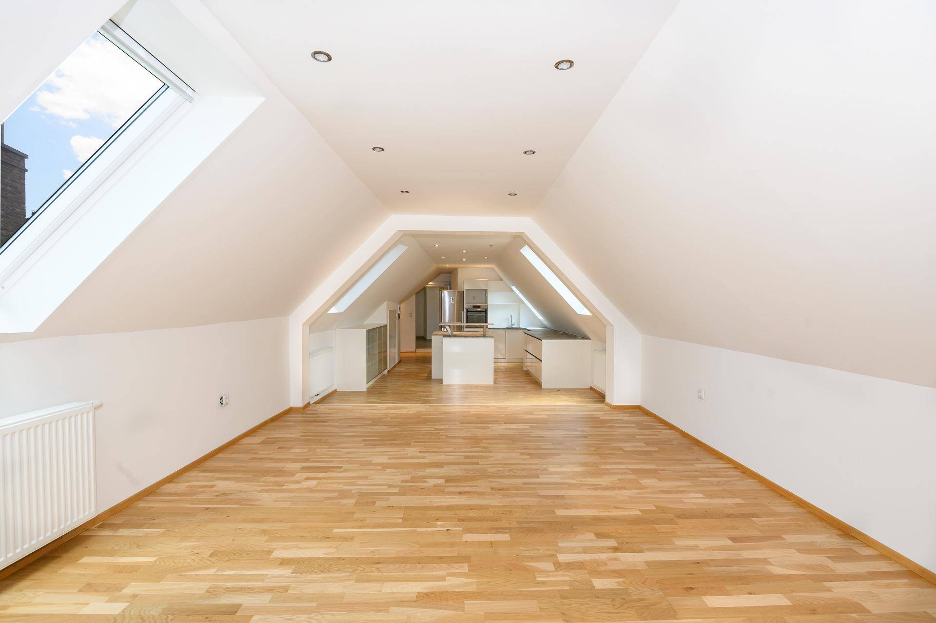Offener Wohnbereich im Dachgeschoss mit Holzboden, Dachfenstern und Blick auf die moderne Küche.