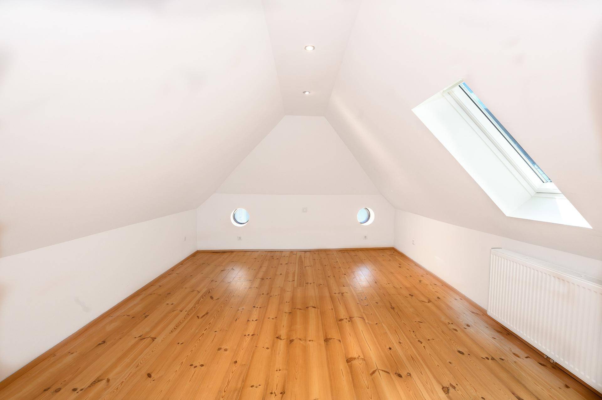 Gemütlicher Dachbodenraum mit Holzboden, runden Fenstern und einem großen Dachfenster für viel Licht.