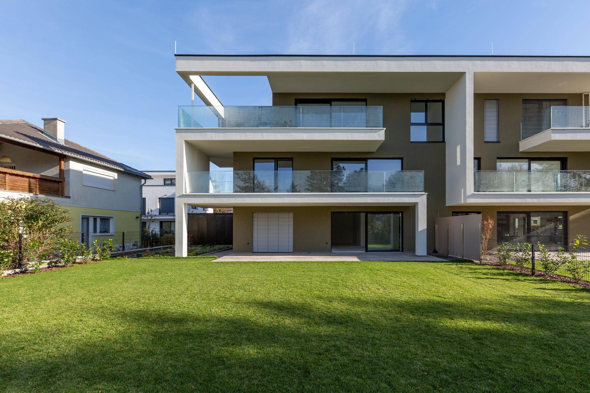Rückansicht eines modernen Wohnhauses mit Balkonen und einer weitläufigen, grünen Rasenfläche.