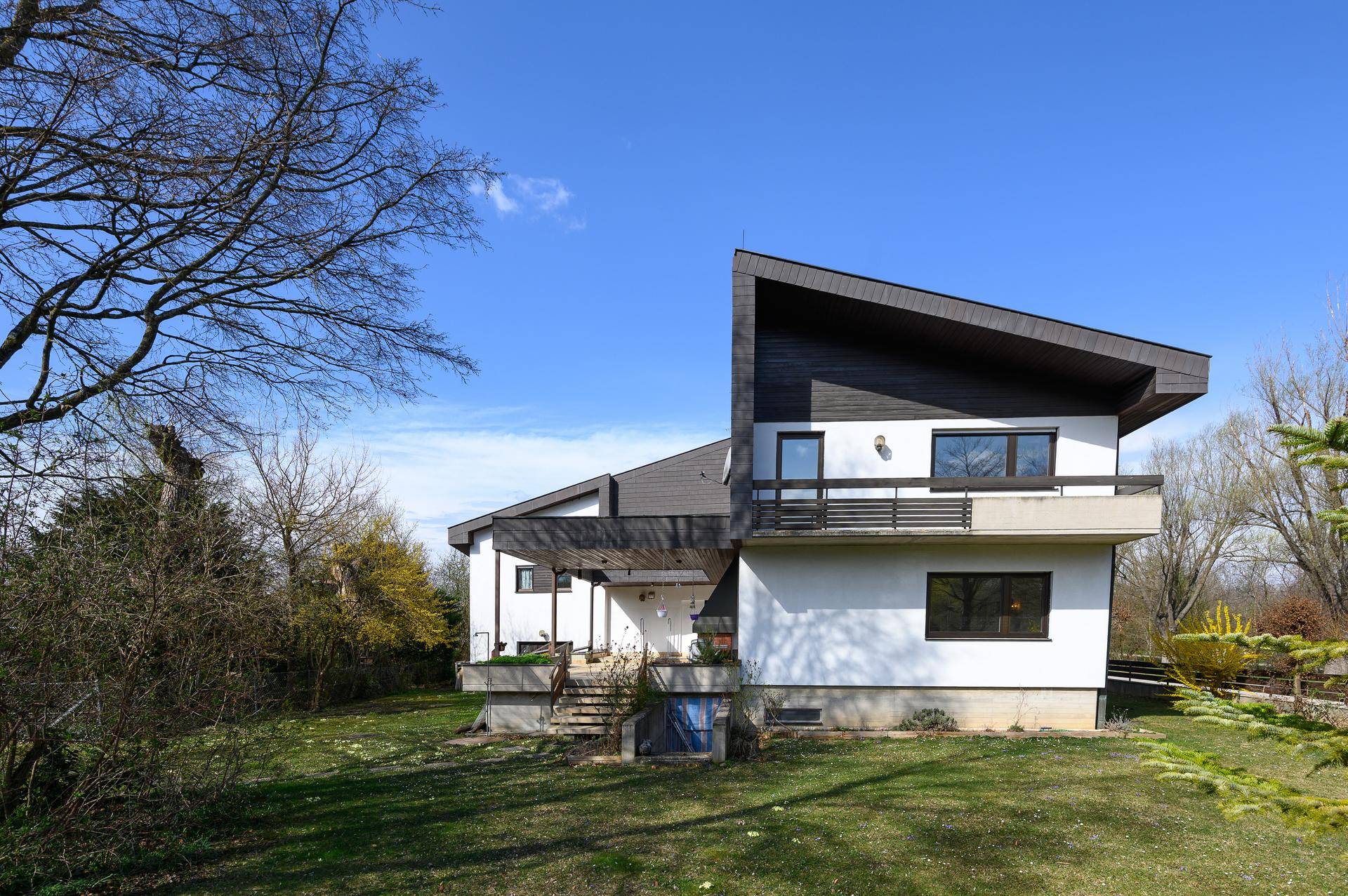 Seitenansicht des Hauses mit großem, gepflegtem Garten und Balkon im Obergeschoss.