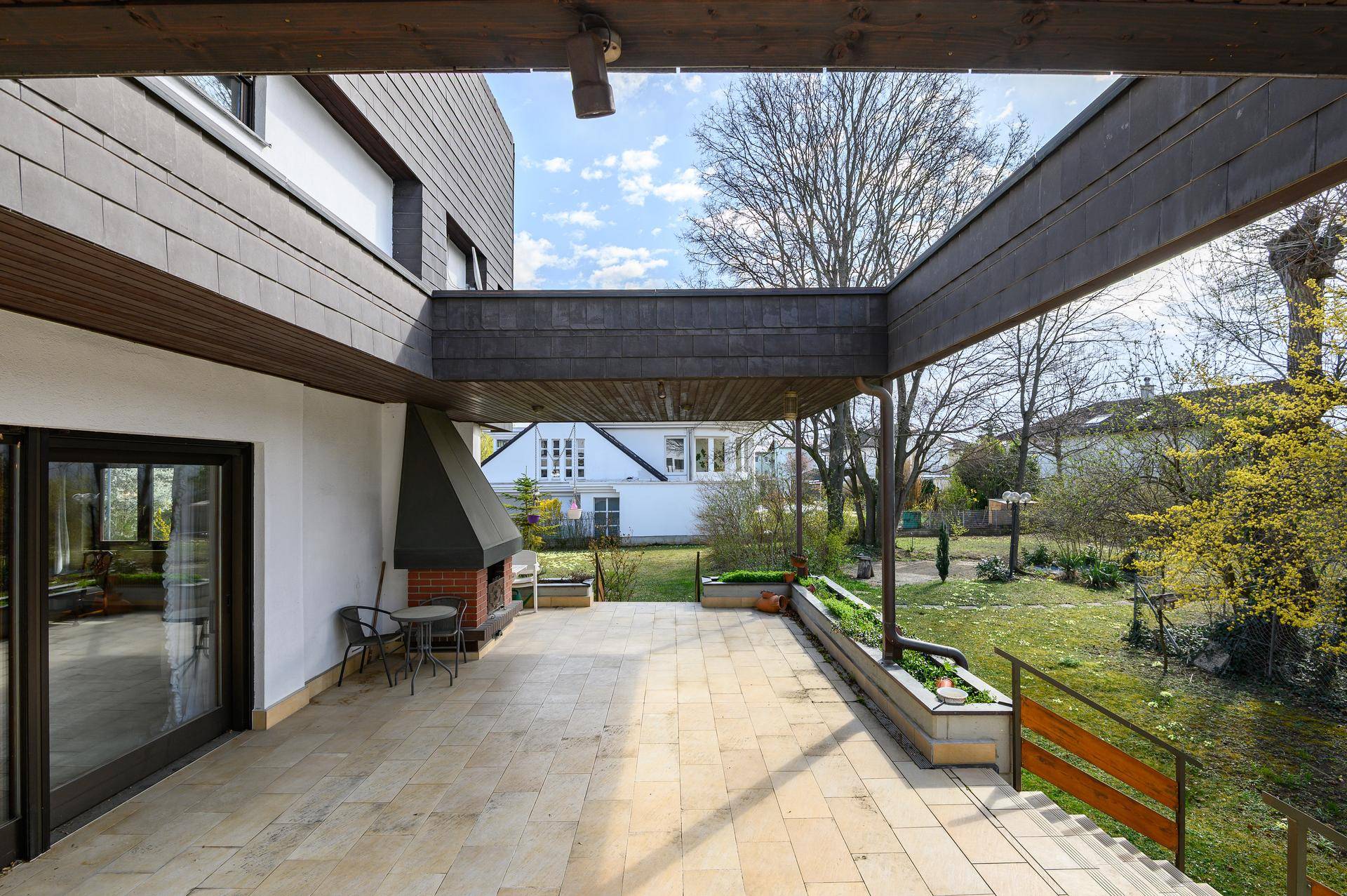 Große überdachte Terrasse mit Außenkamin und weitem Blick in den grünen Garten.