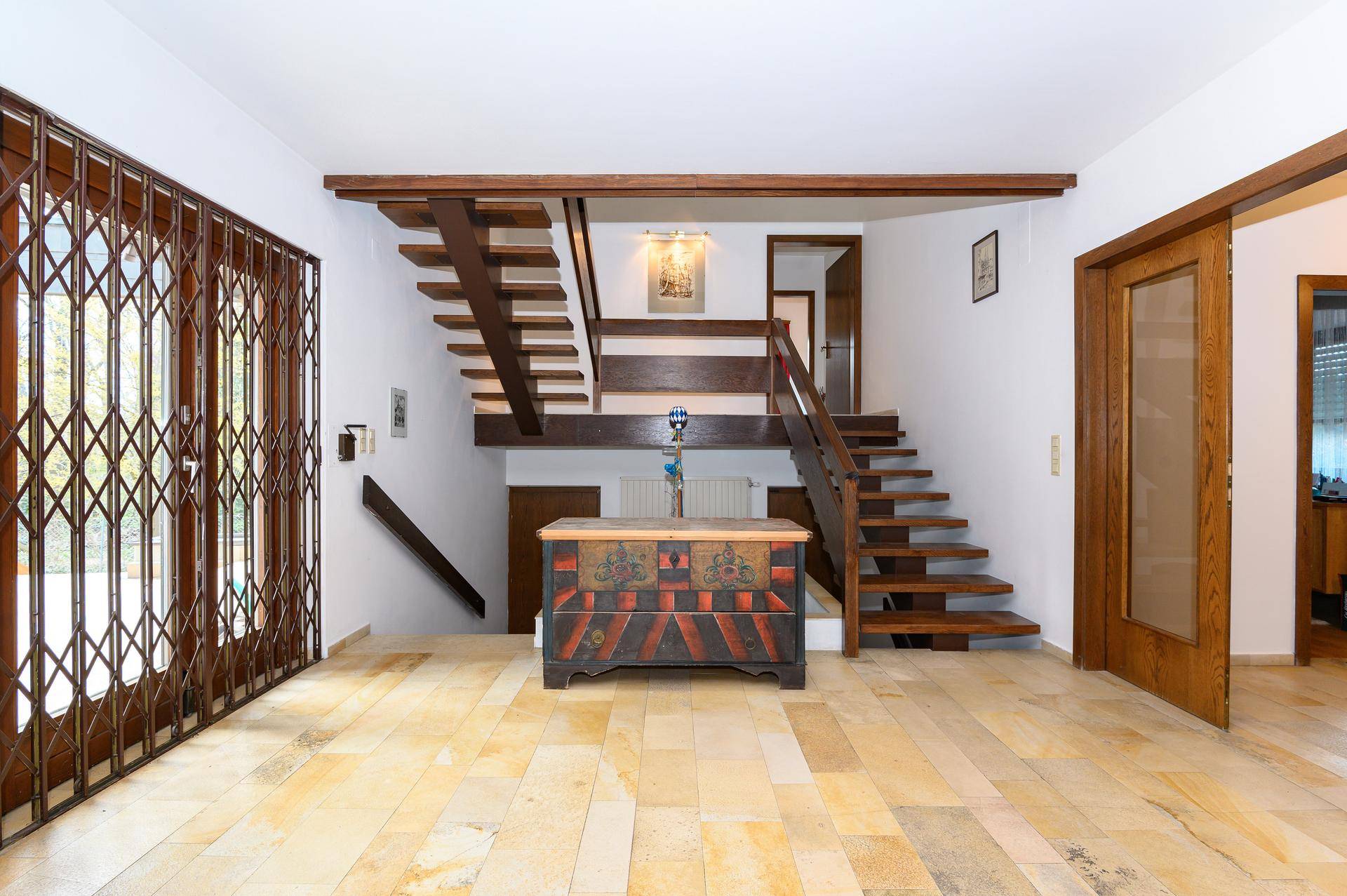 Geräumiger Eingangsbereich mit offener Holztreppe, Fliesenboden und dekorativer Truhe.
