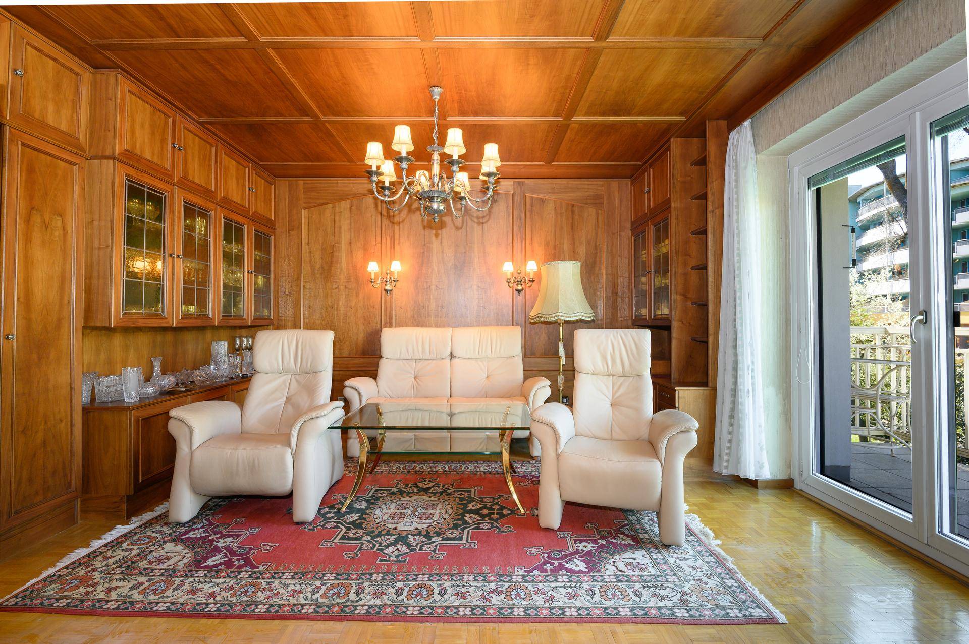 Gemütliches Wohnzimmer mit Holzvertäfelung, Ledersofas und Zugang zum Balkon.