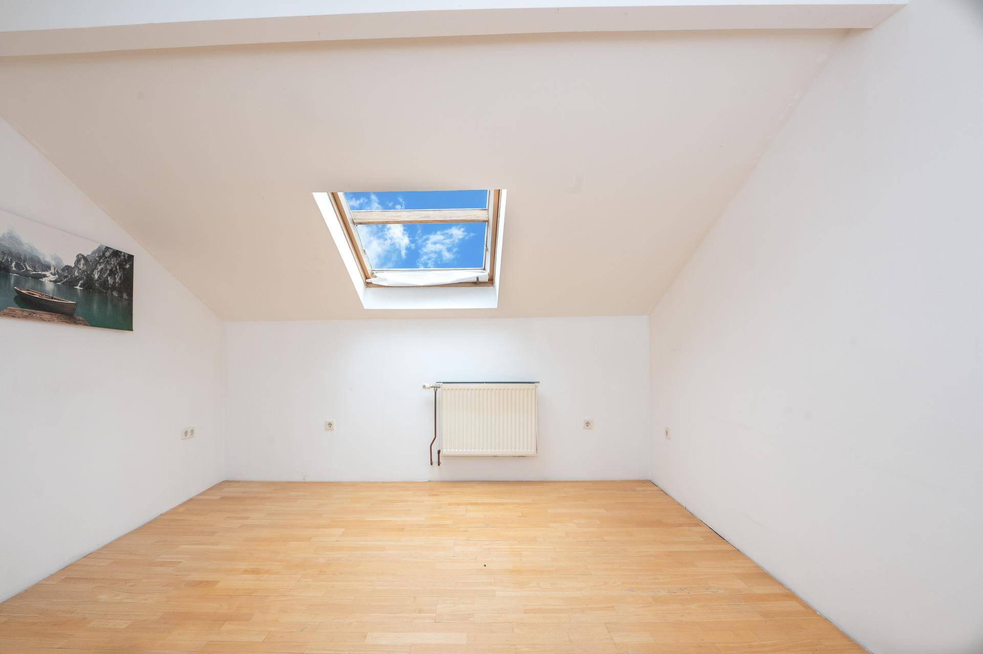 Geräumiges Dachzimmer mit Laminatboden, weiß gestrichenen Wänden und einem großen Dachfenster.