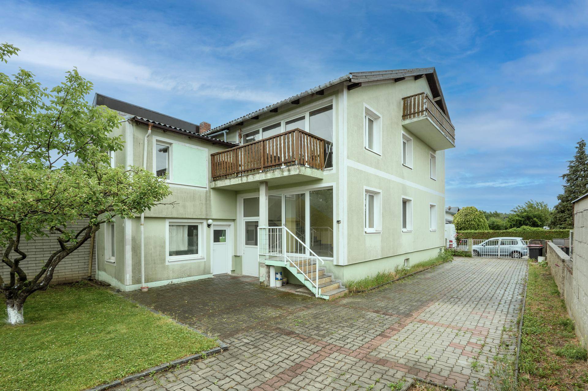 Rückseite des Hauses mit gepflasterter Zufahrt, Rasenfläche und mehreren Balkonen.