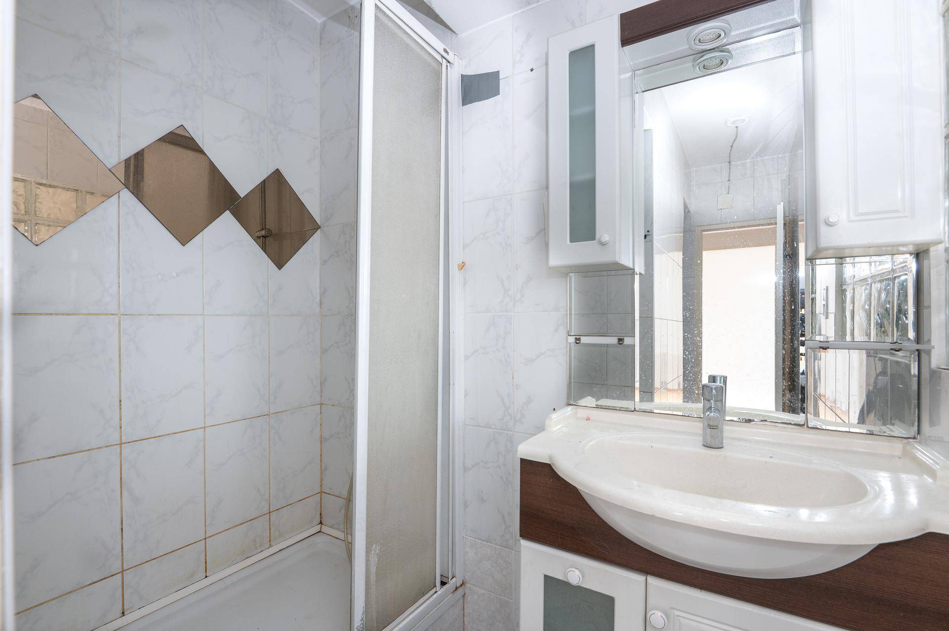 Badezimmer mit Duschkabine, Waschbecken, Spiegelschrank und hellen Fliesen an den Wänden.