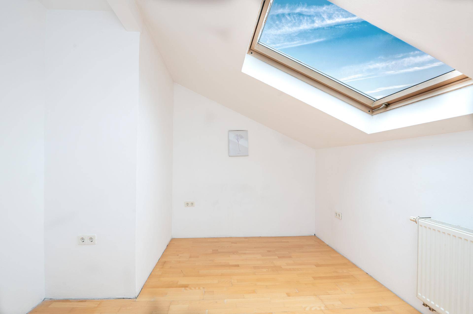 Helles Dachzimmer mit Laminatboden, weiß gestrichenen Wänden und einem großen Dachfenster.