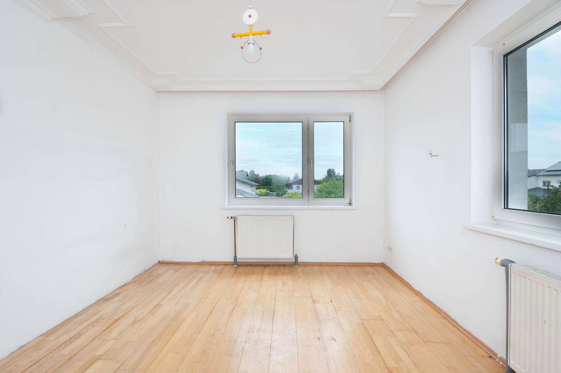Geräumiges Zimmer mit Holzdielenboden, weiß gestrichenen Wänden und zwei großen Fenstern.