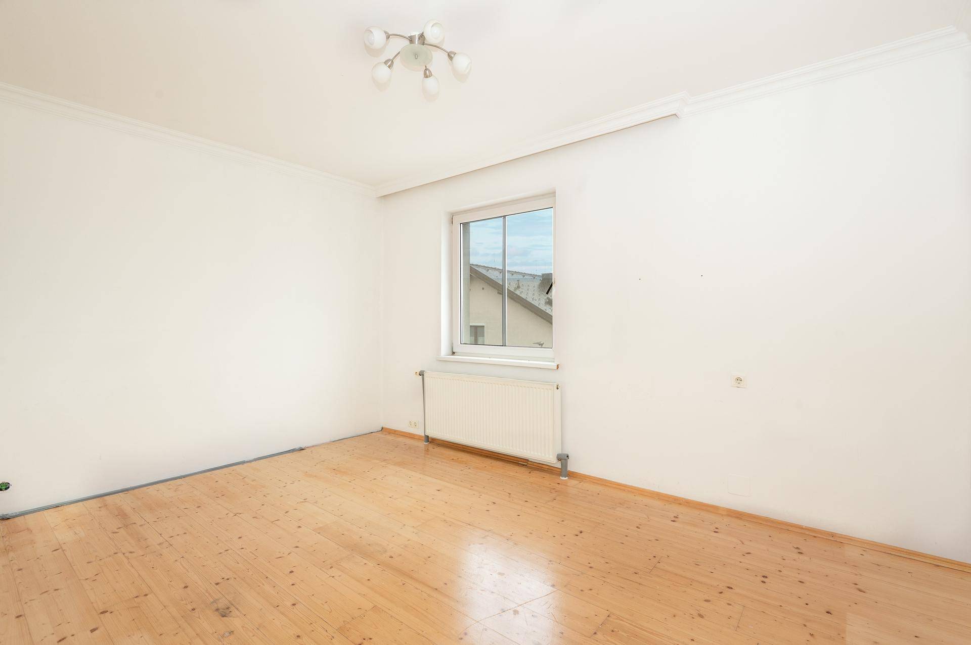 Leeres Zimmer mit hellem Holzdielenboden, weiß gestrichenen Wänden und einem Fenster.