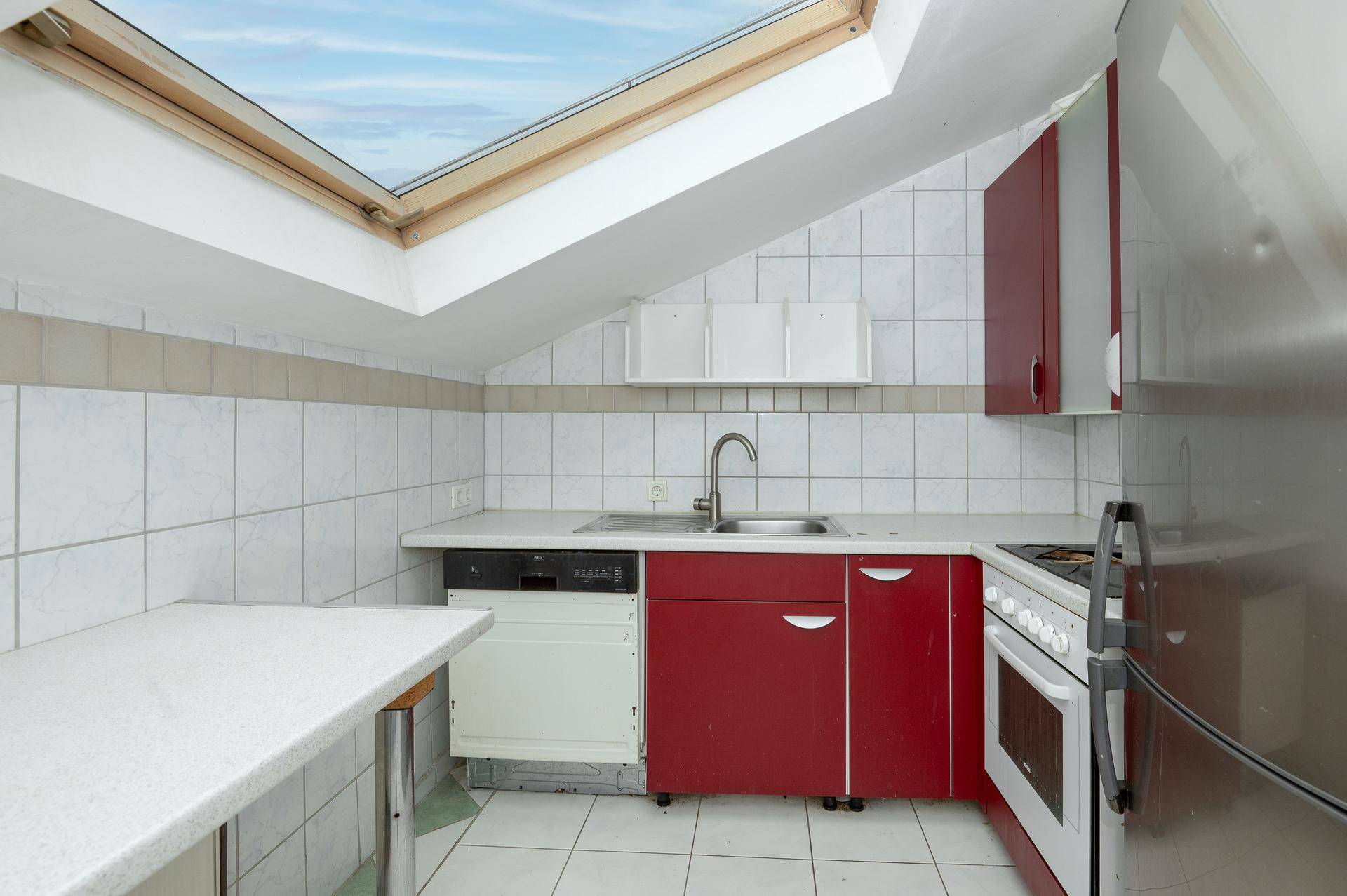Dachgeschossküche mit roten Unterschränken, Fliesenboden, Dachfenster und Geschirrspüler.