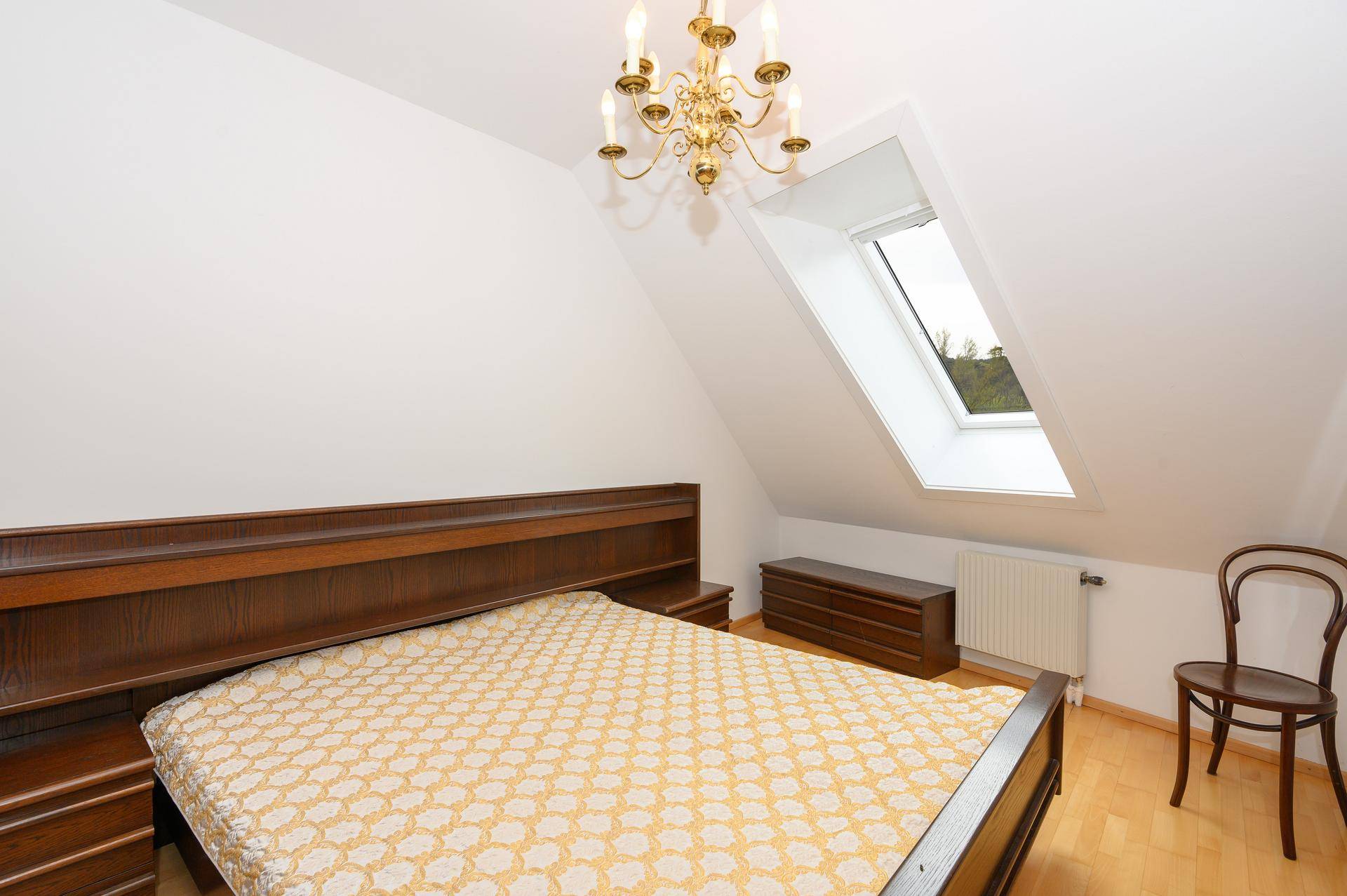 Schlafzimmer mit Holzbett, Kommode und Dachfenster, das viel Tageslicht in den Raum lässt.