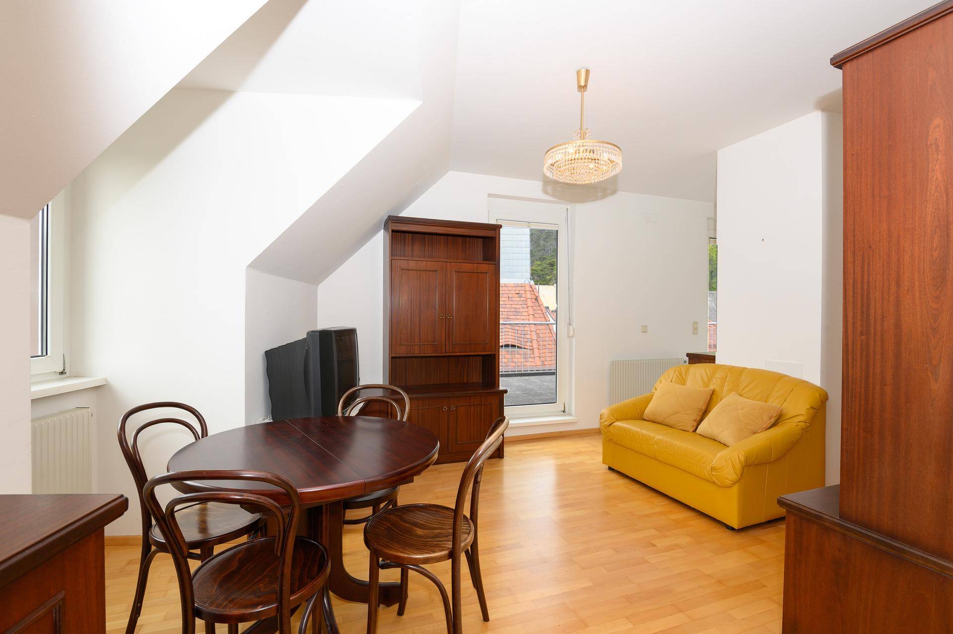 Heller Wohn-Essbereich mit gelbem Sofa, Esstisch und traditionellen Holzmöbeln im Dachgeschoss.