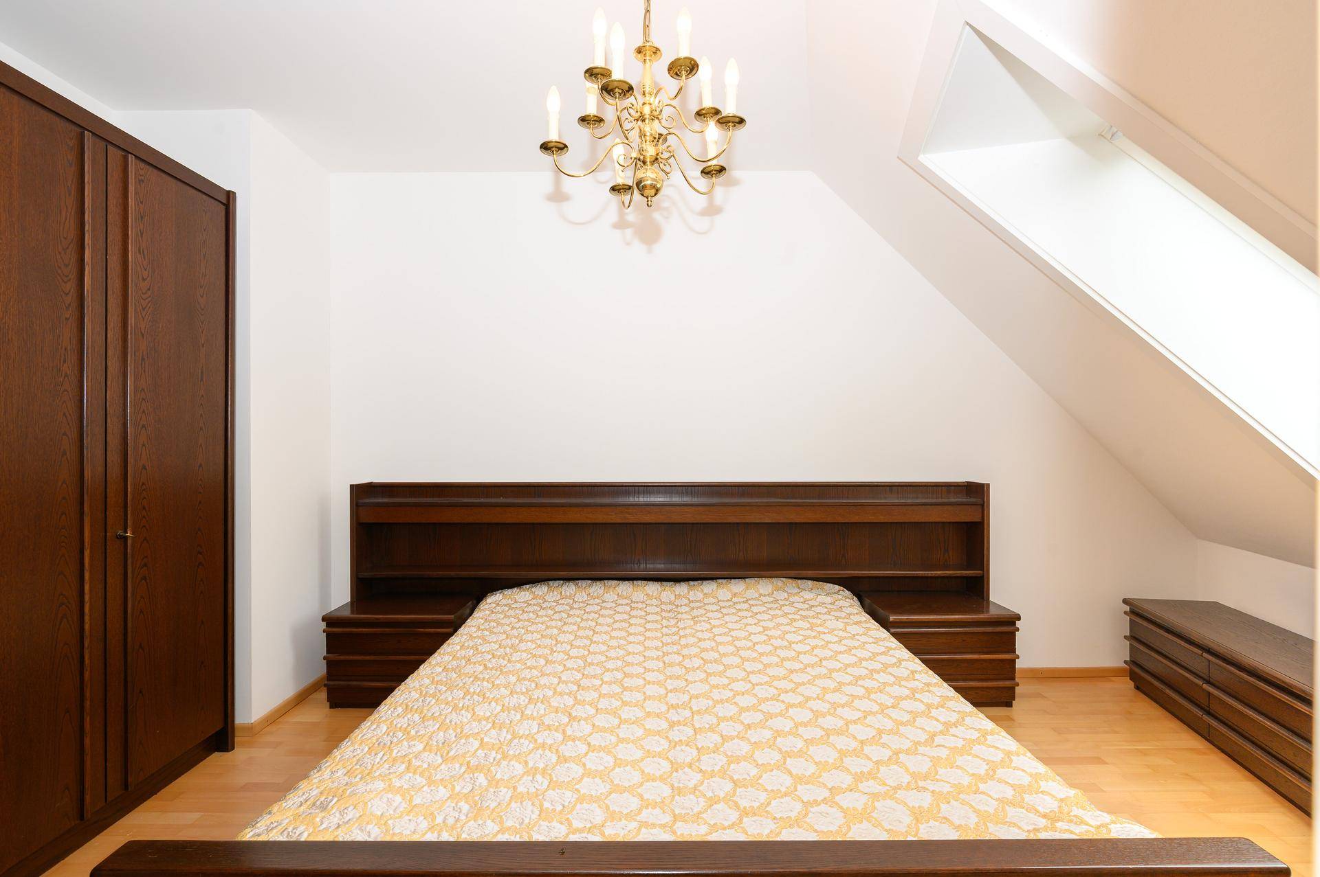 Schlafzimmer im Dachgeschoss mit großem Holzbett, Kleiderschrank und einem Dachfenster für natürliches Licht.