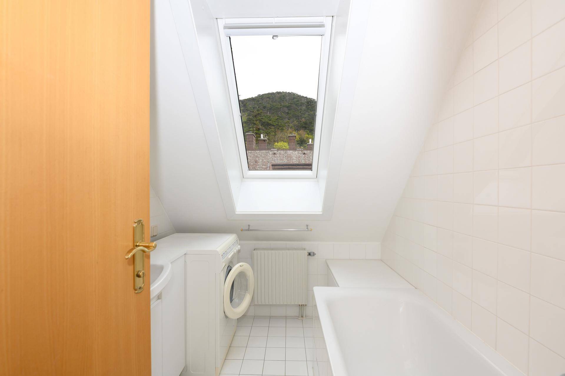 Badezimmer mit Badewanne, Waschmaschine, Fliesenboden und einem Dachfenster für Tageslicht.