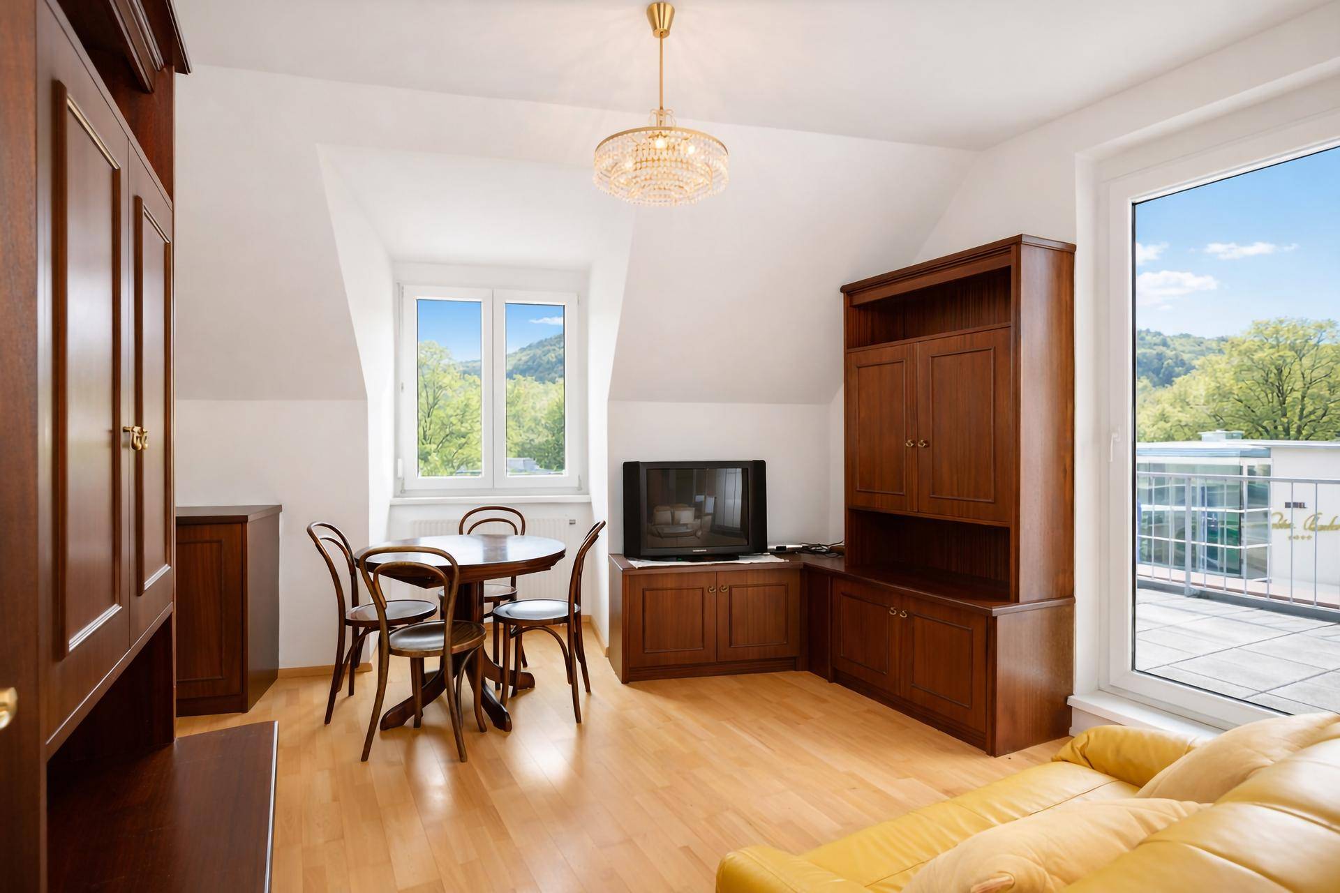 Gemütlicher Wohn-Essbereich im Dachgeschoss mit Holzboden, gelbem Sofa und Zugang zur Terrasse.
