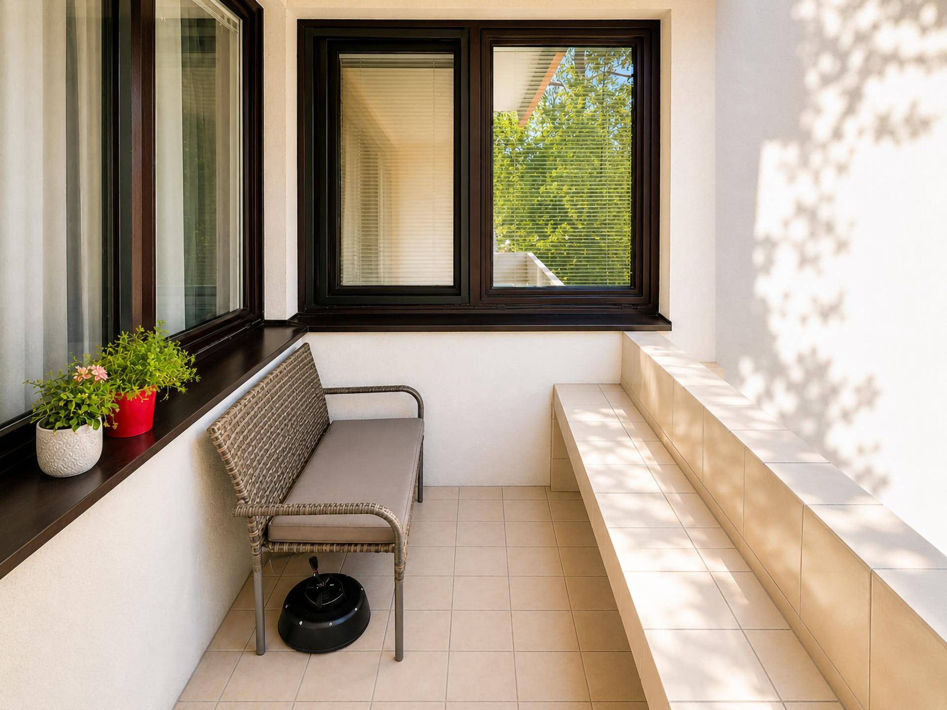 Kleiner, sonniger Balkon mit Fliesenboden, Sitzbank und Topfpflanzen.