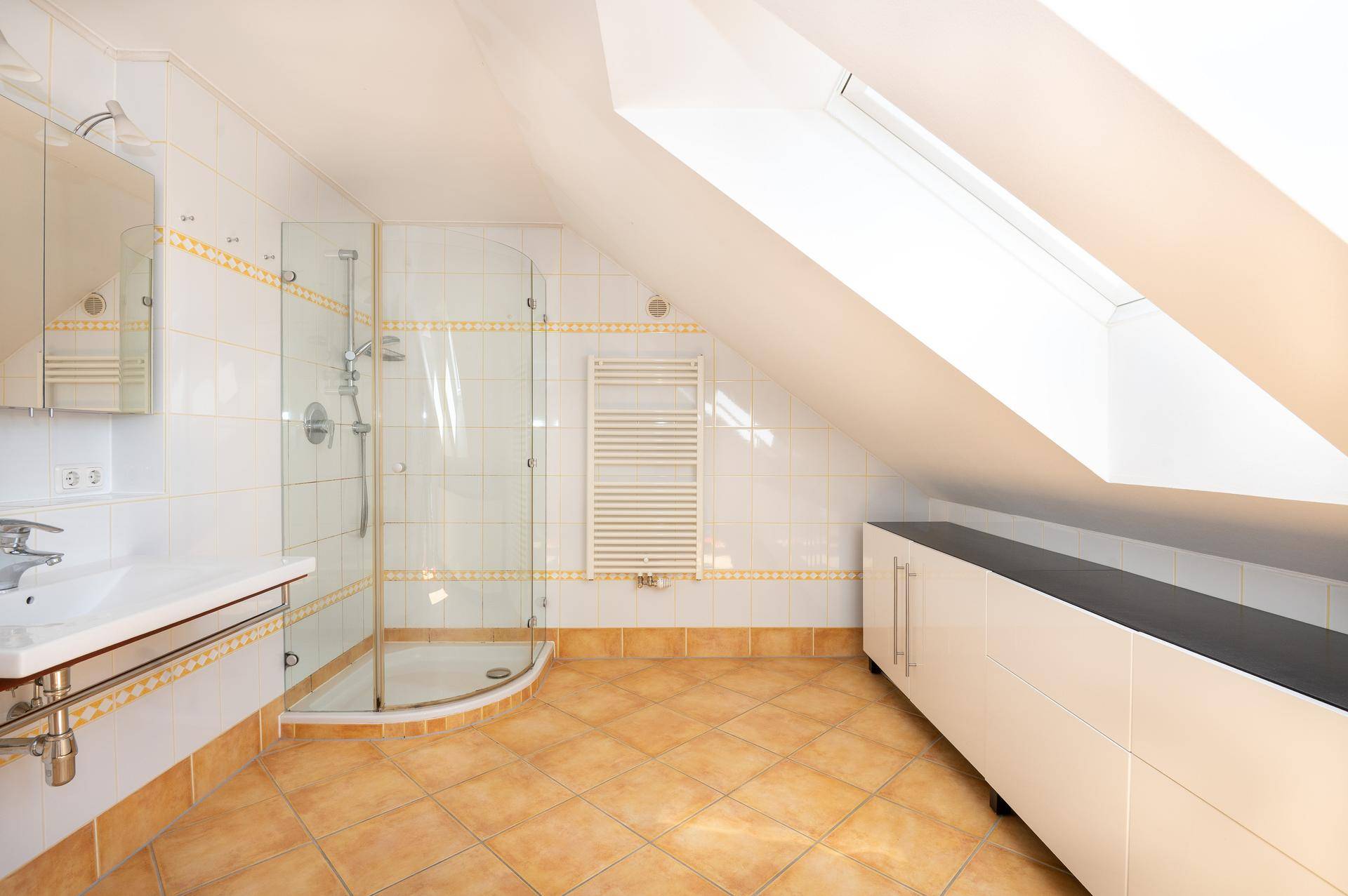 Dachgeschoss-Badezimmer mit Dusche, Waschbecken, Fliesen und Dachfenster.