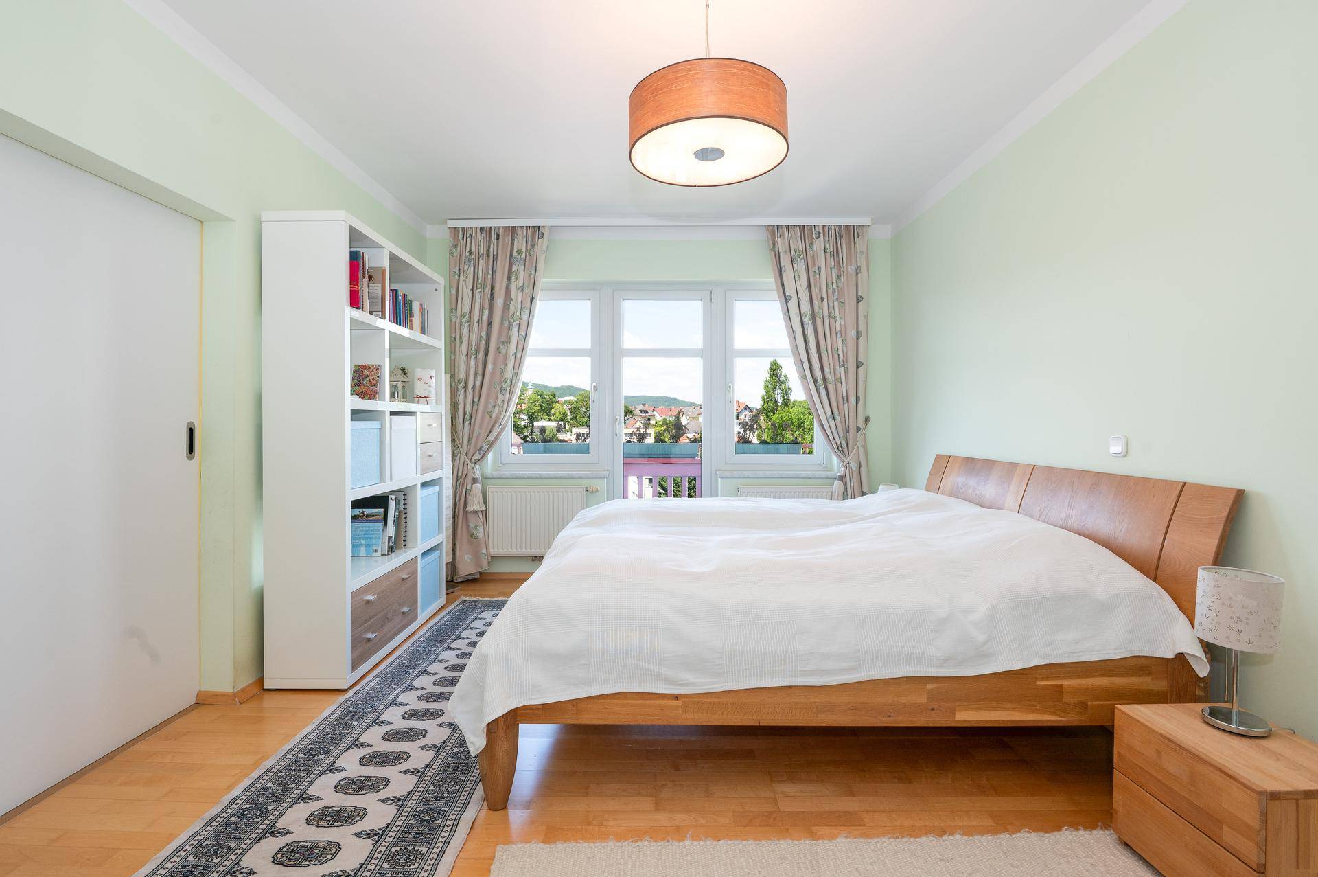 Helles Schlafzimmer mit Holzbett, hellgrünen Wänden und Blick auf die Stadt.