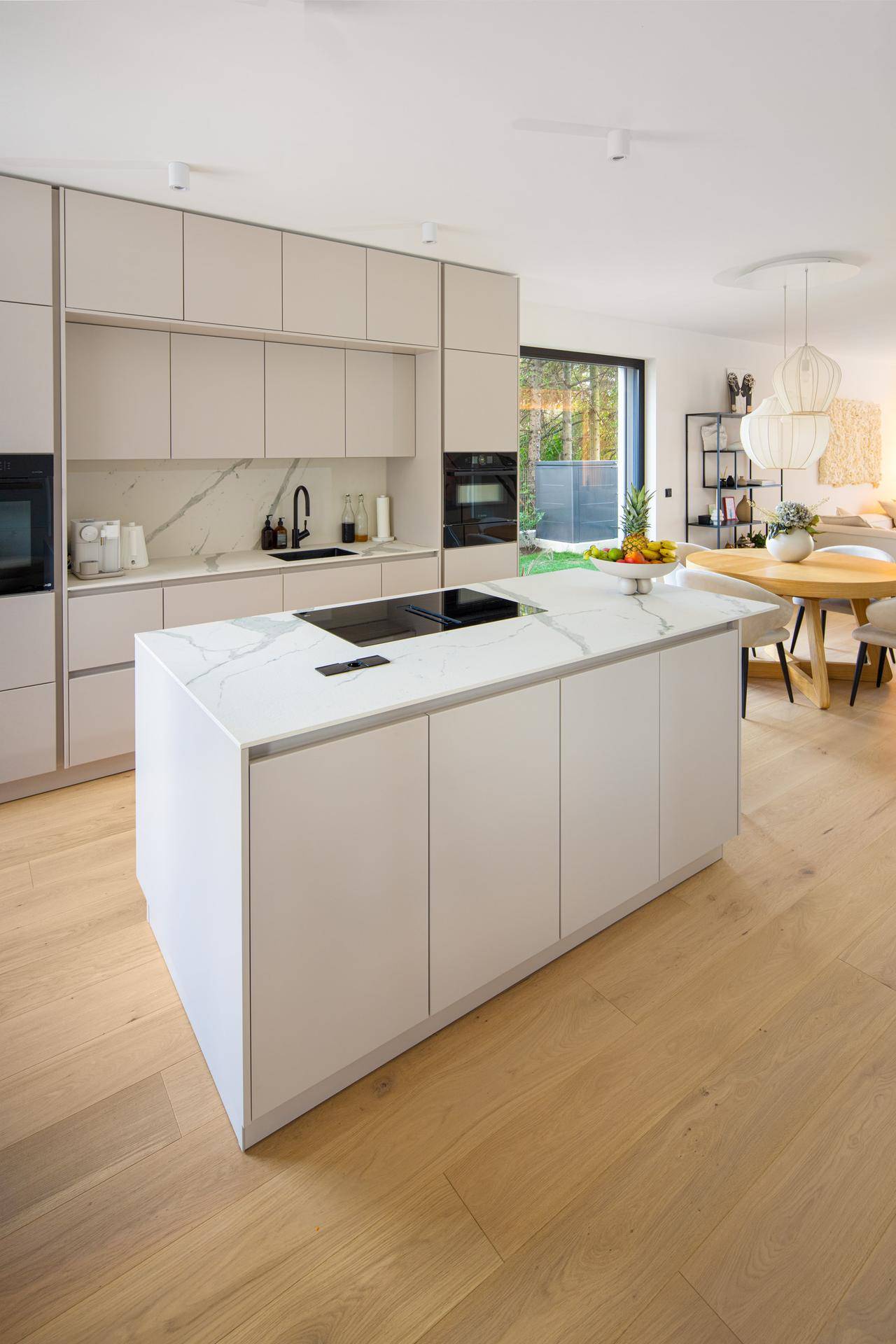 Offene, moderne Küche mit Kochinsel, hellen Fronten und Essbereich mit Holzboden.