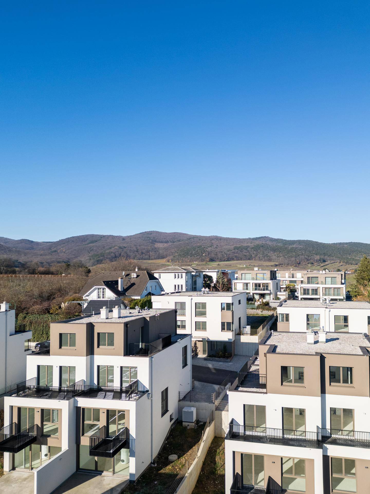 Moderne Wohnanlage mit mehreren Gebäuden in einer grünen Hügellandschaft unter blauem Himmel.
