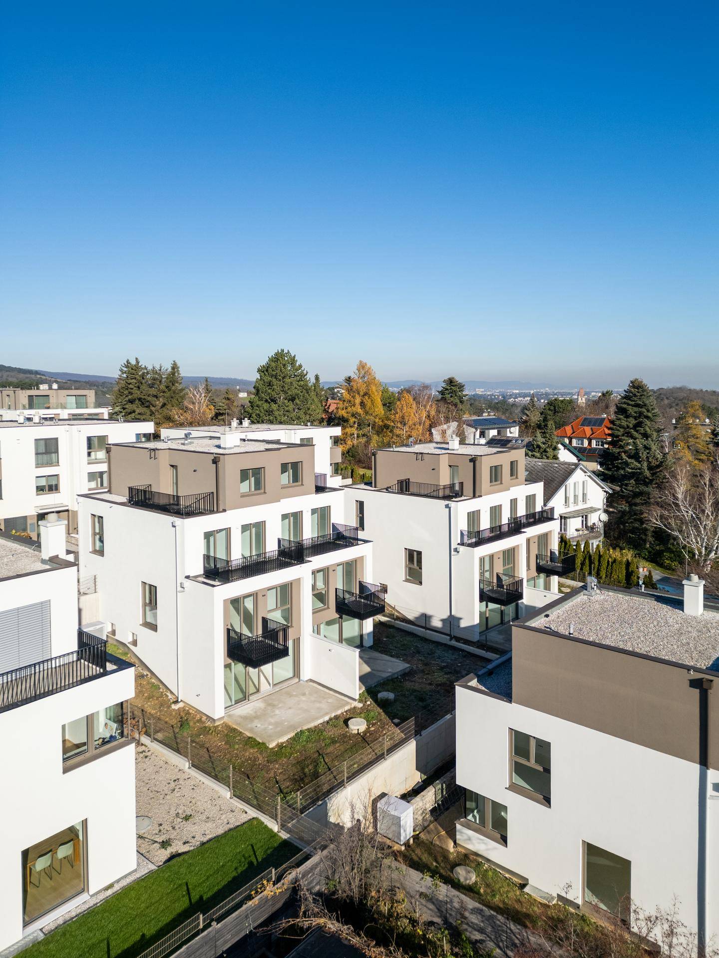 Moderne Wohngebäude mit Flachdächern und Balkonen in einer Siedlung unter blauem Himmel.