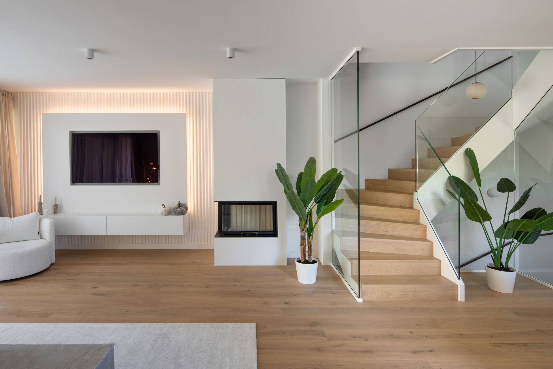 Helles Wohnzimmer mit modernem Kamin, Holzfußboden und offener Treppe mit Glasgeländer.