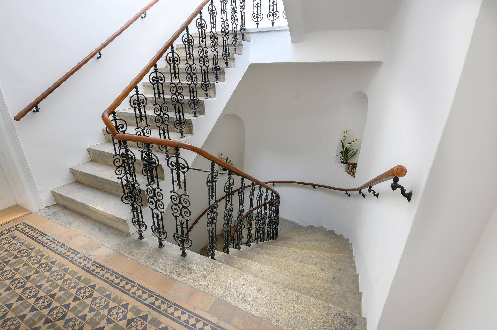 Elegantes Treppenhaus mit schmiedeeisernem Geländer und gemusterten Bodenfliesen in einem Altbau.