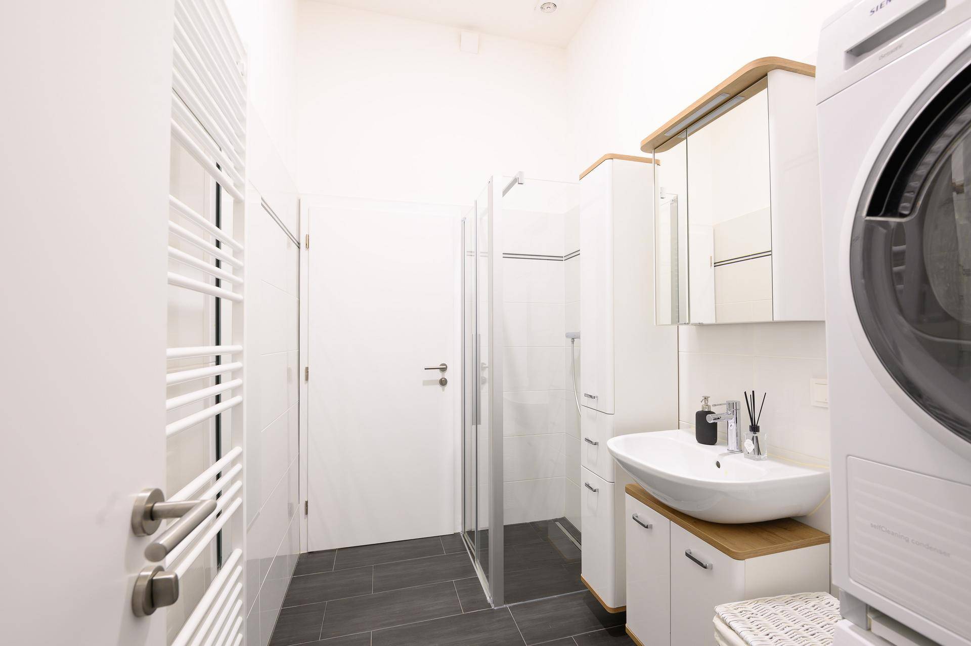 Modernes Badezimmer mit Dusche, Waschmaschine und dunklen Bodenfliesen.