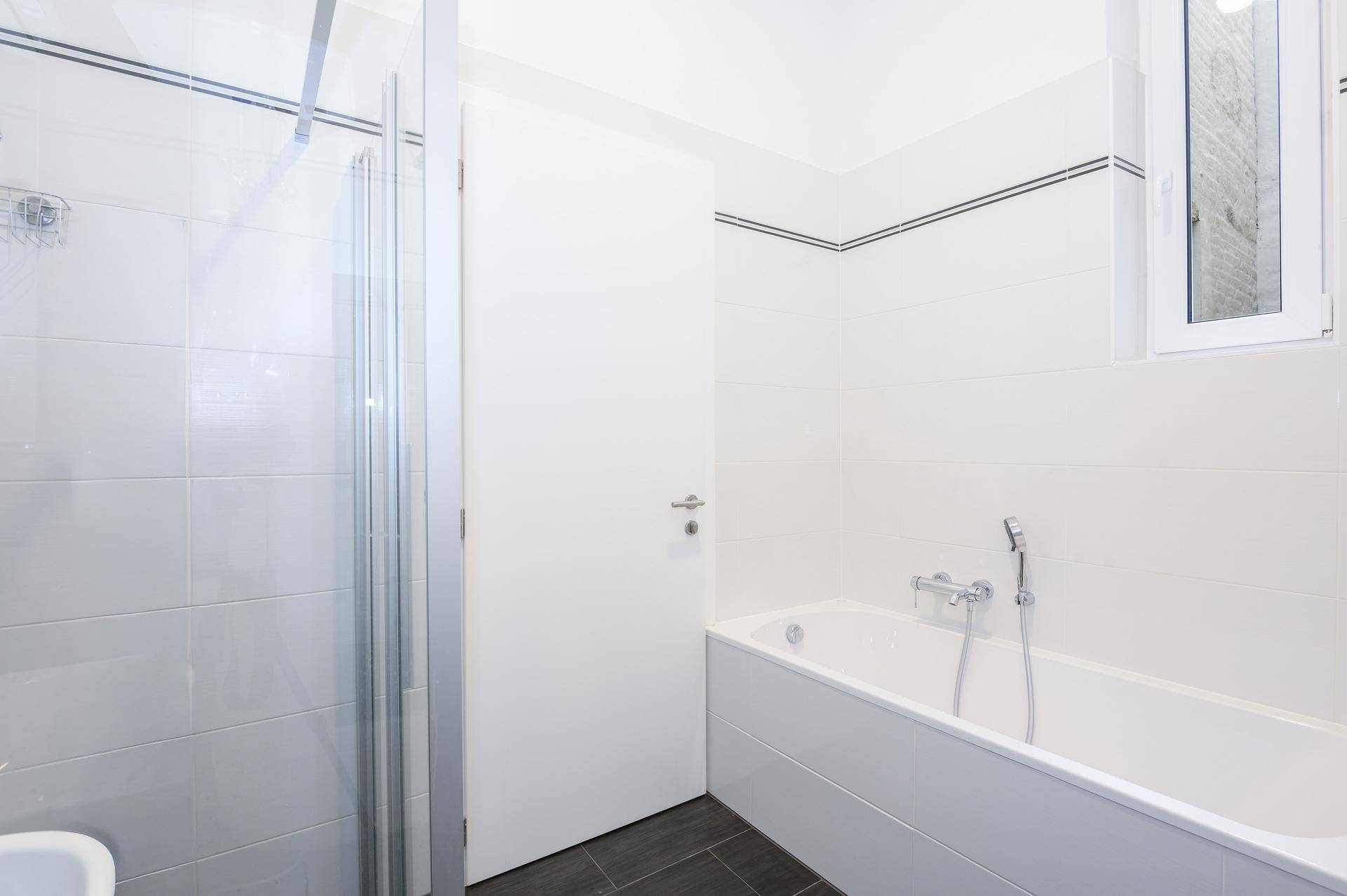 Helles Badezimmer mit Badewanne, Dusche und Fenster für natürliche Belüftung.