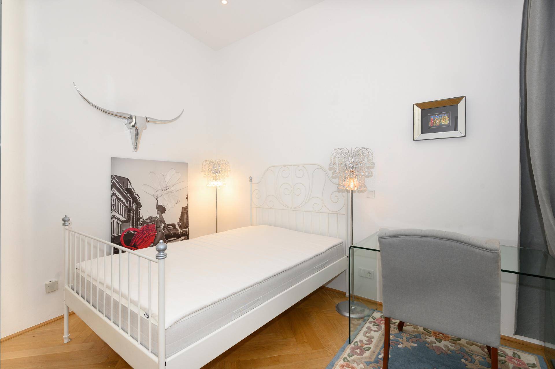 Helles Schlafzimmer mit weißem Metallbett, Parkettboden und modernen Stehlampen.