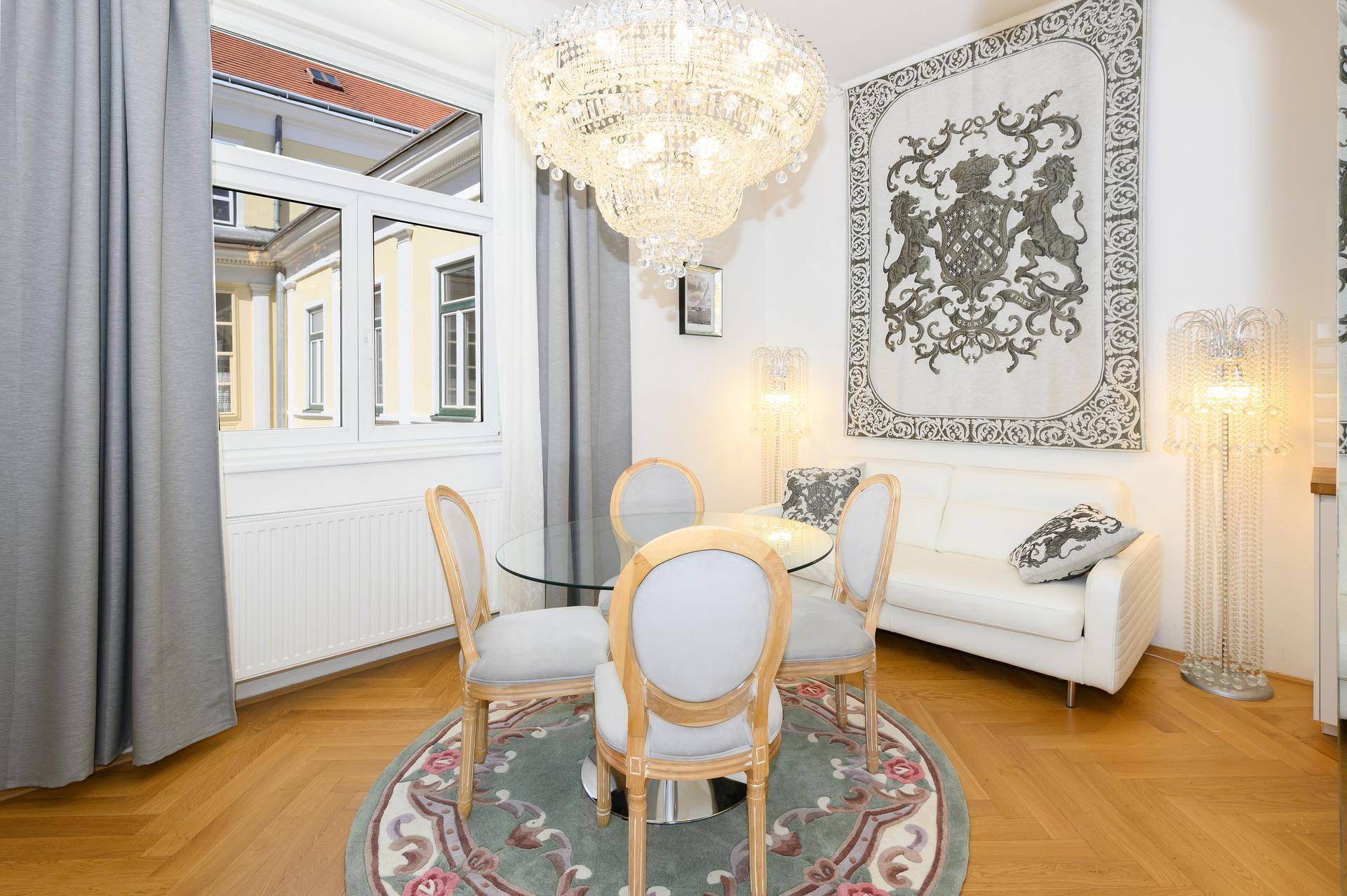 Heller Essbereich mit großem Fenster, Kronleuchter und klassischem Teppich auf Parkettboden.