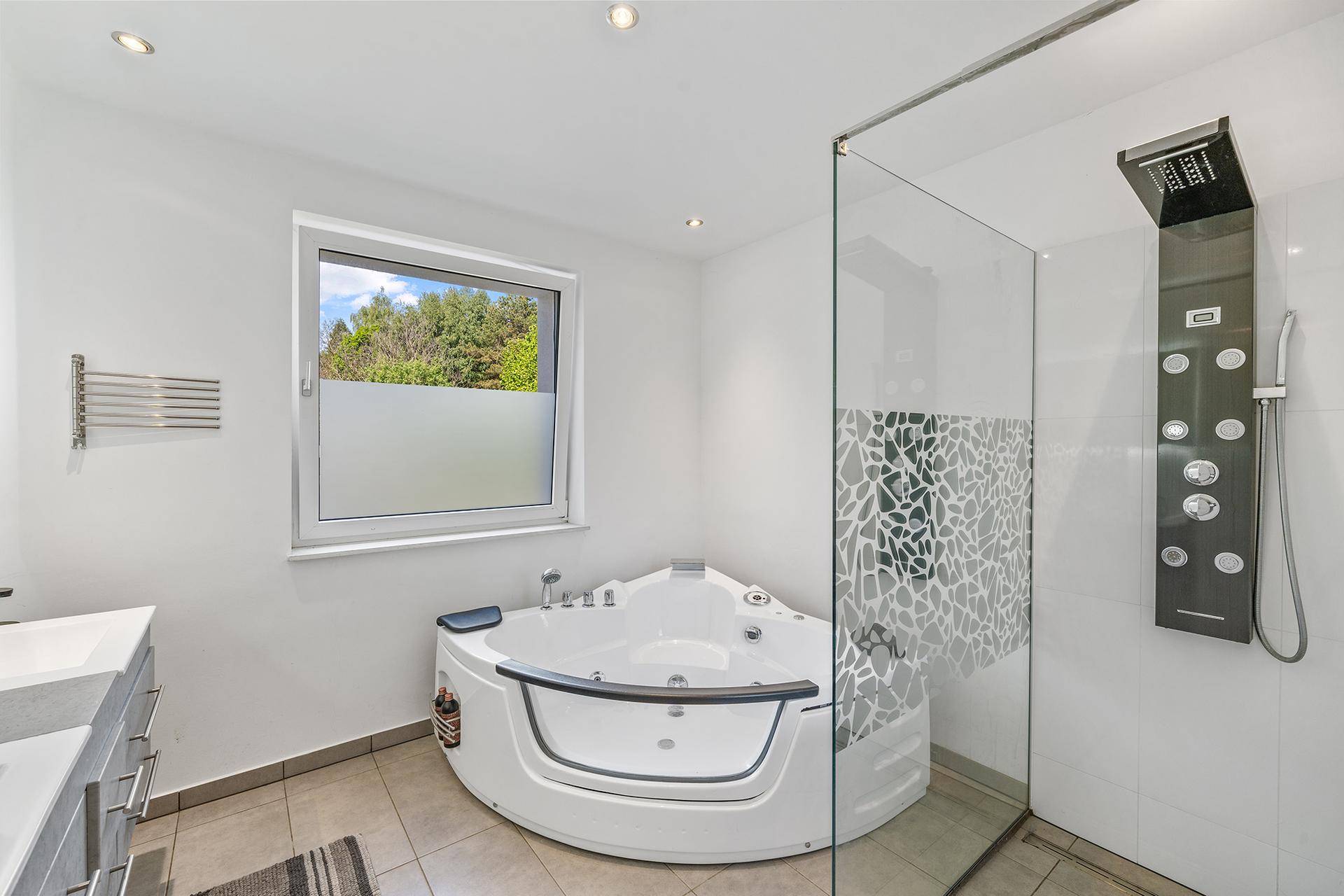 Modernes Badezimmer mit Eck-Whirlpool, großer Dusche und Fenster.