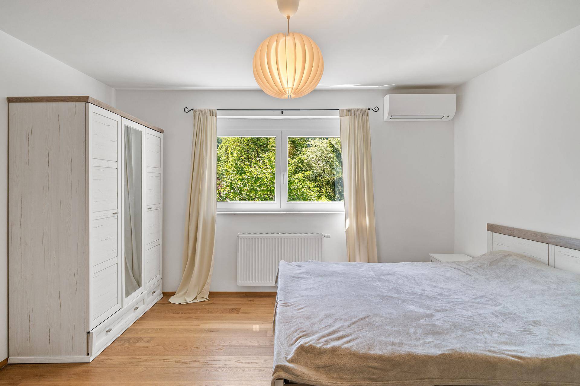 Helles Schlafzimmer mit Holzboden, Klimaanlage und Blick ins Grüne.