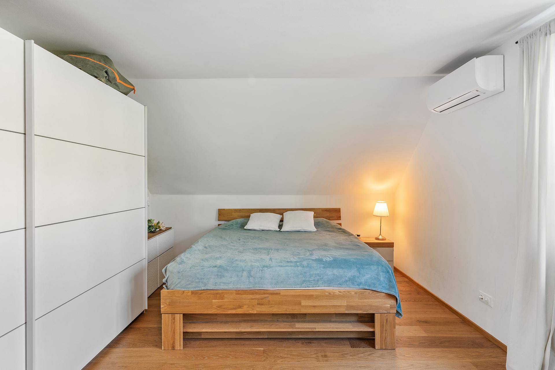 Gemütliches Schlafzimmer im Dachgeschoss mit Holzbett und Klimaanlage.