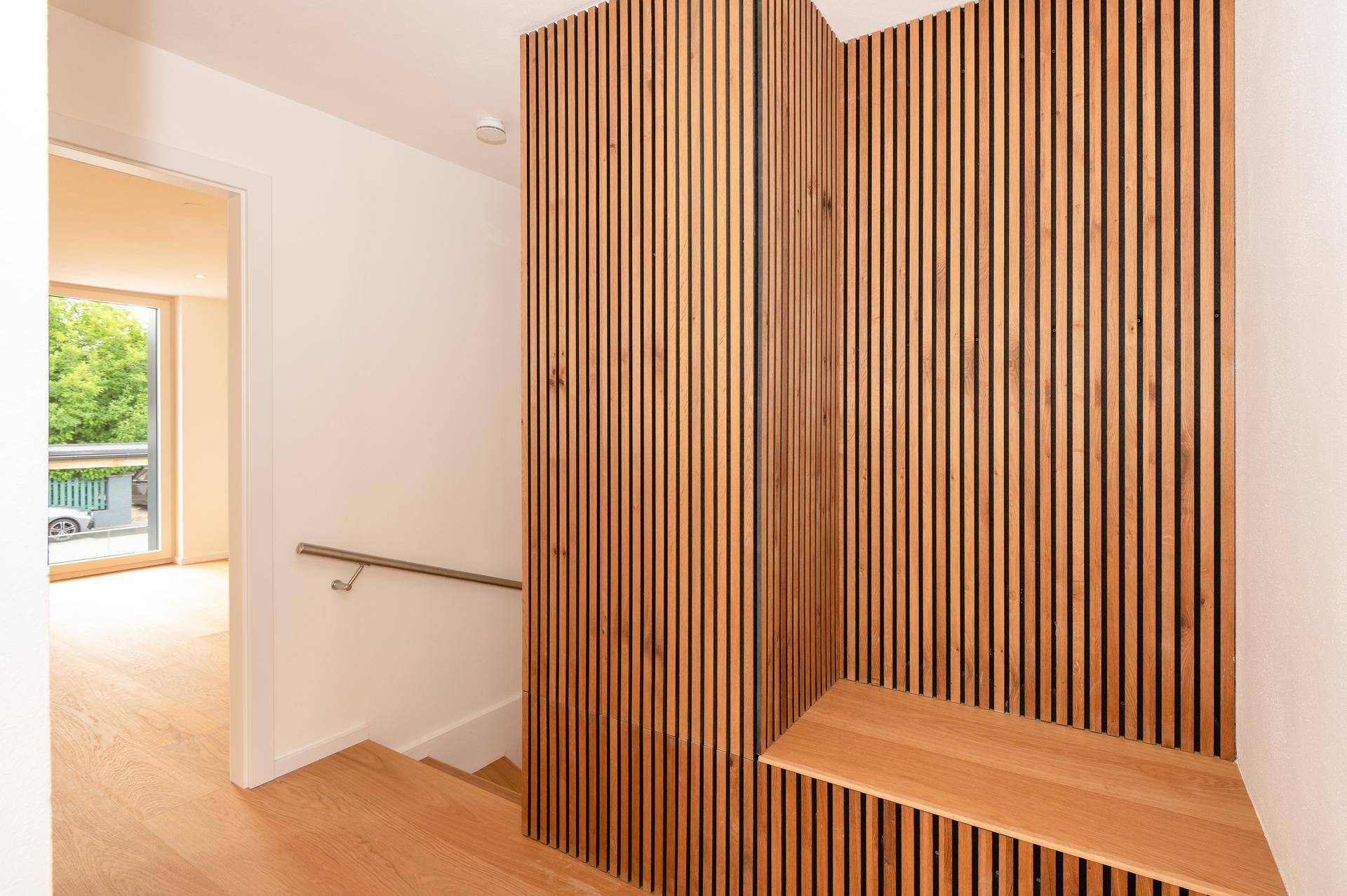 Treppenbereich mit Holzstufen und moderner Holzlamellenwand, die zum Obergeschoss führt.
