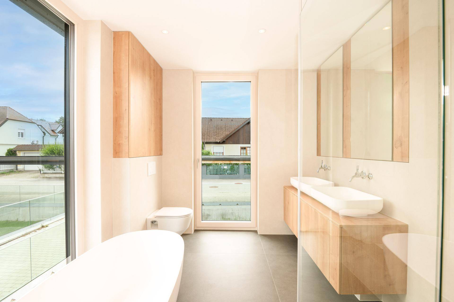 Modernes Badezimmer mit freistehender Badewanne, Doppelwaschbecken und großen Fenstern.